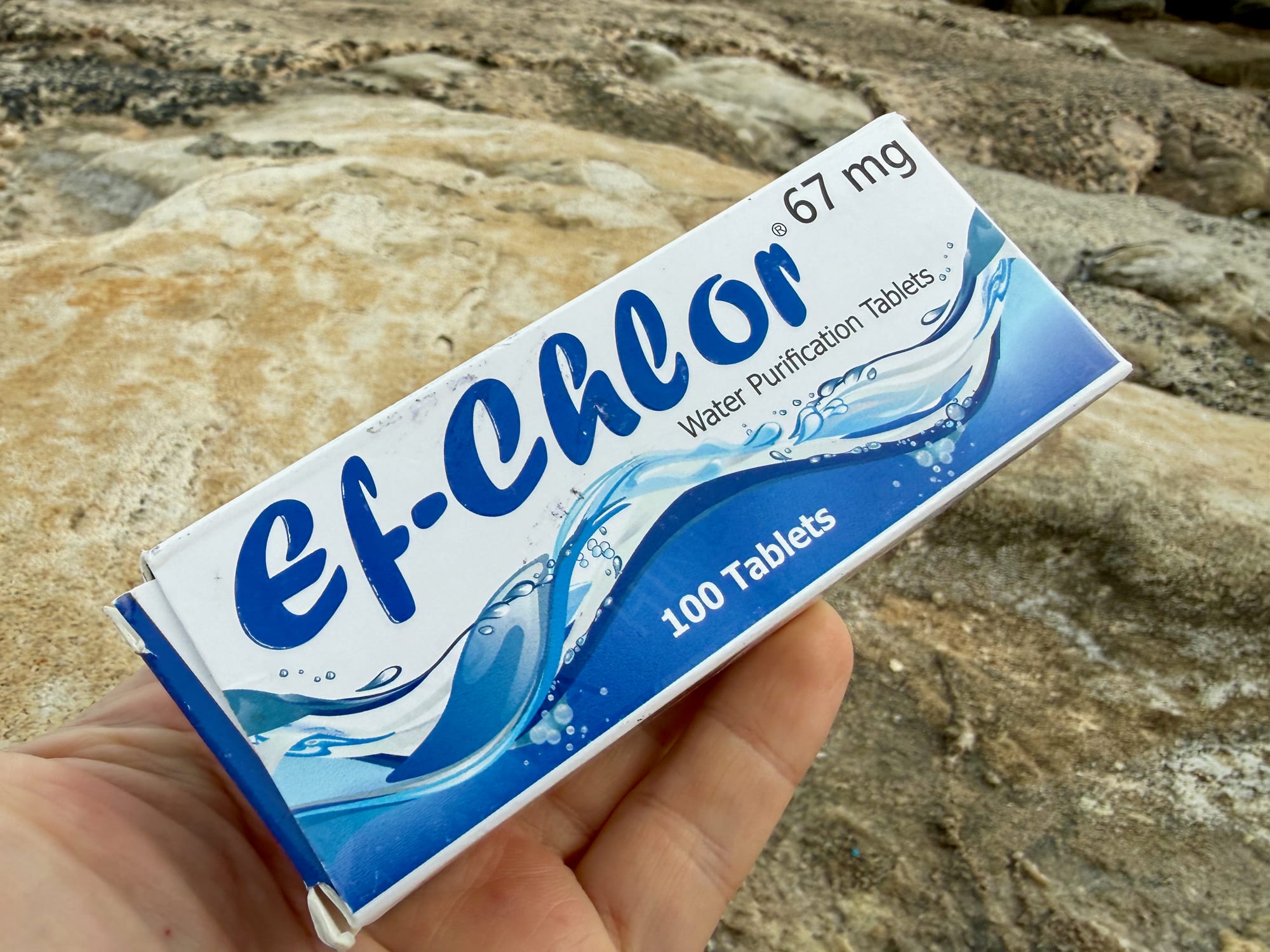 A hand holding the box of Ef-Chlor Water Purification Tablets