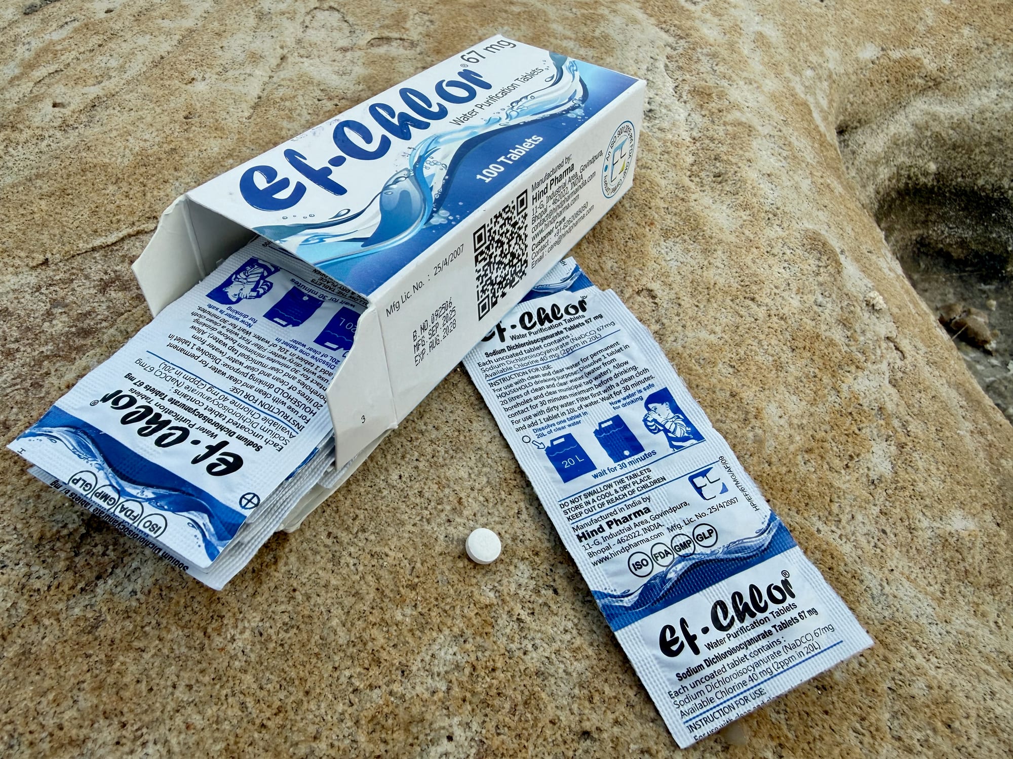 An open box of Ef-Chlor tablets with foil strips pulled out and one small white tablet on the rock