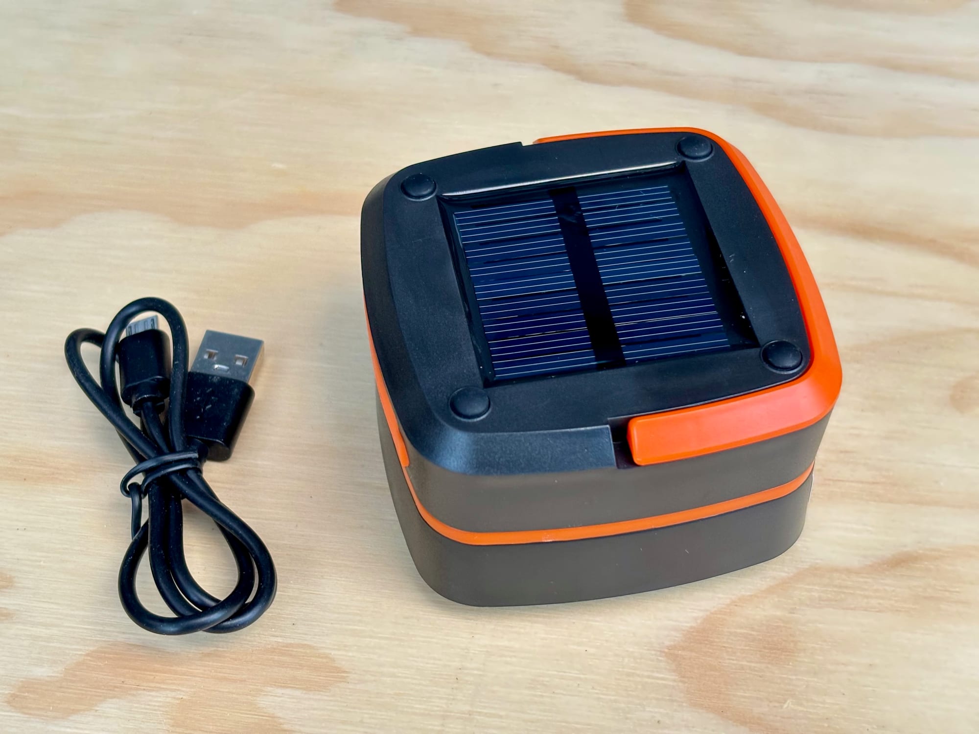 The folded solar lantern with its solar panel on top, next to its USB cable