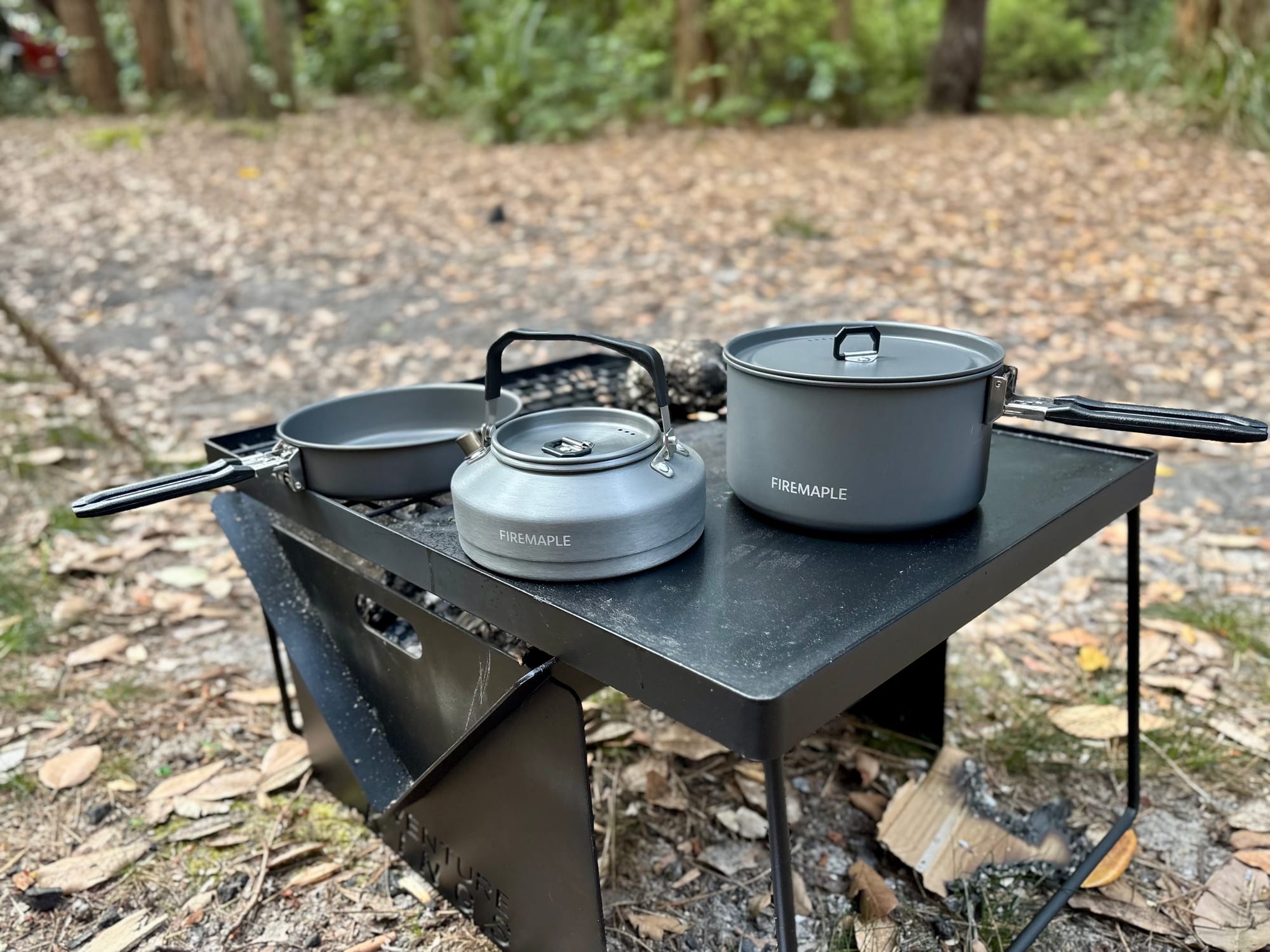 Firemaple Feast 2 cookware set: frypan, kettle and pot on a camp table