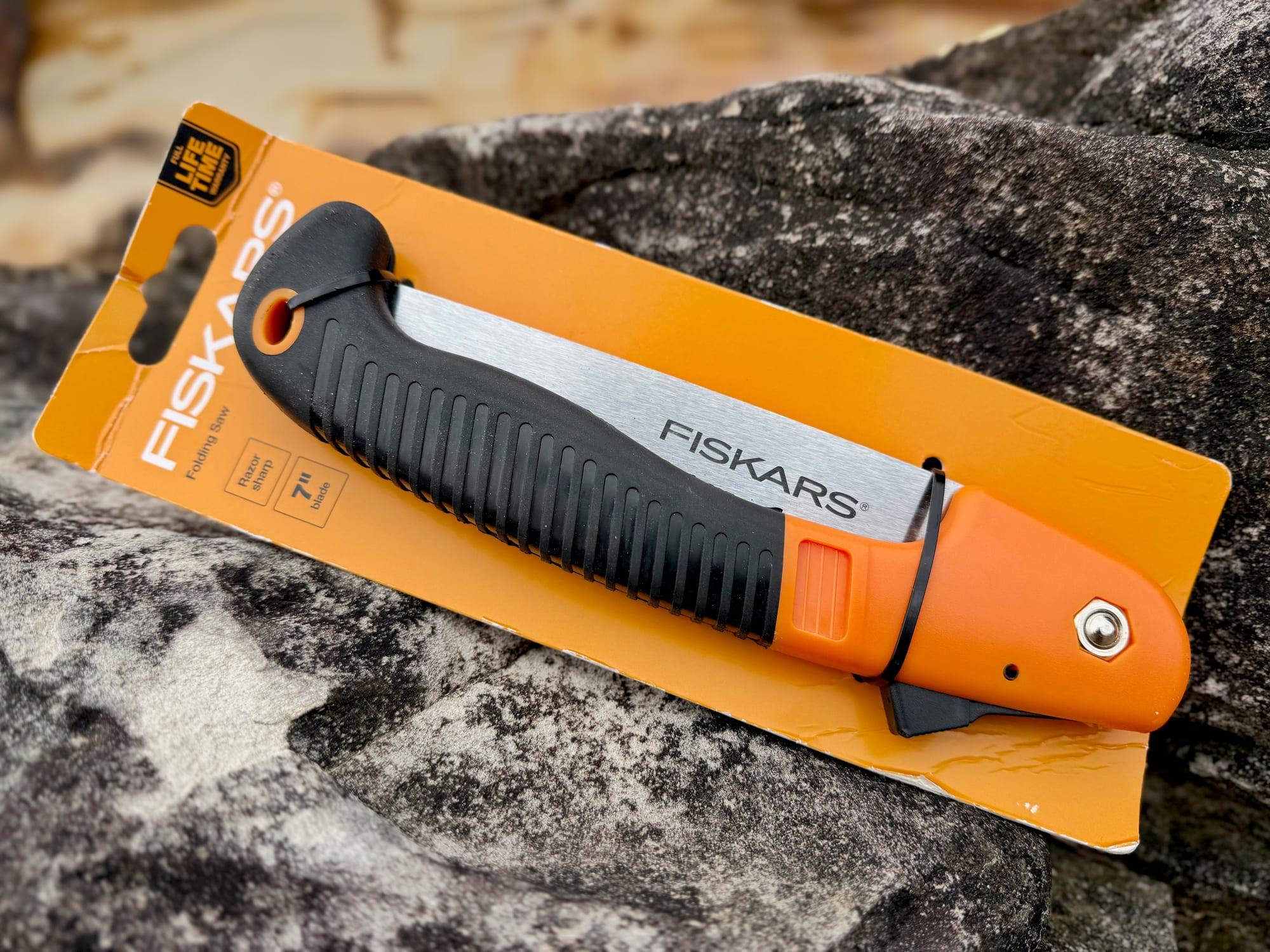 The Fiskars 7-inch folding saw in its orange packaging on a rock