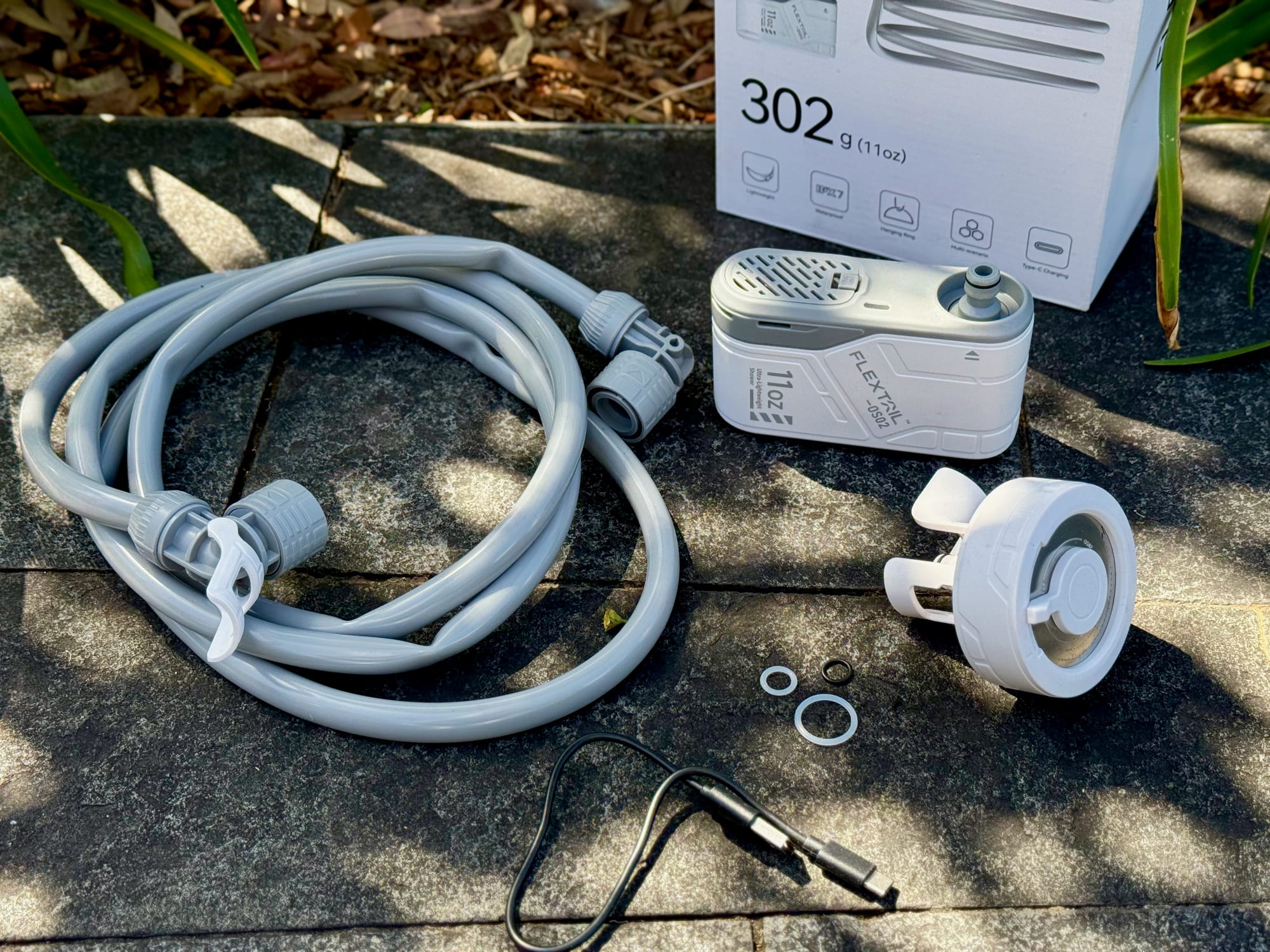 The FlexTail Max Shower pump, hose, shower head, charging cable and spare O-rings laid out in front of the box