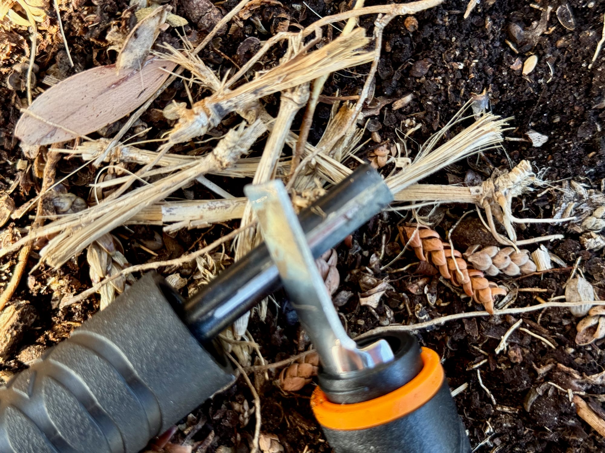 The striker of the Gerber Fire Starter held against the ferro rod over a pile of dry grass