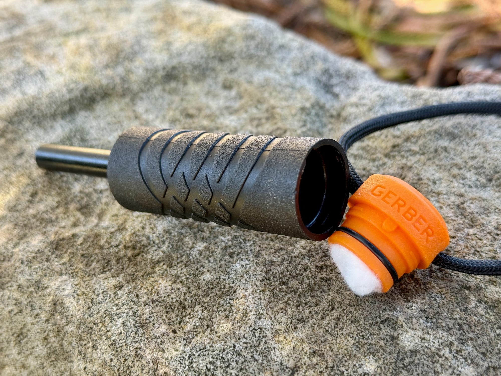 The tinder compartment of the Gerber Fire Starter open, with a cotton ball on the orange cap