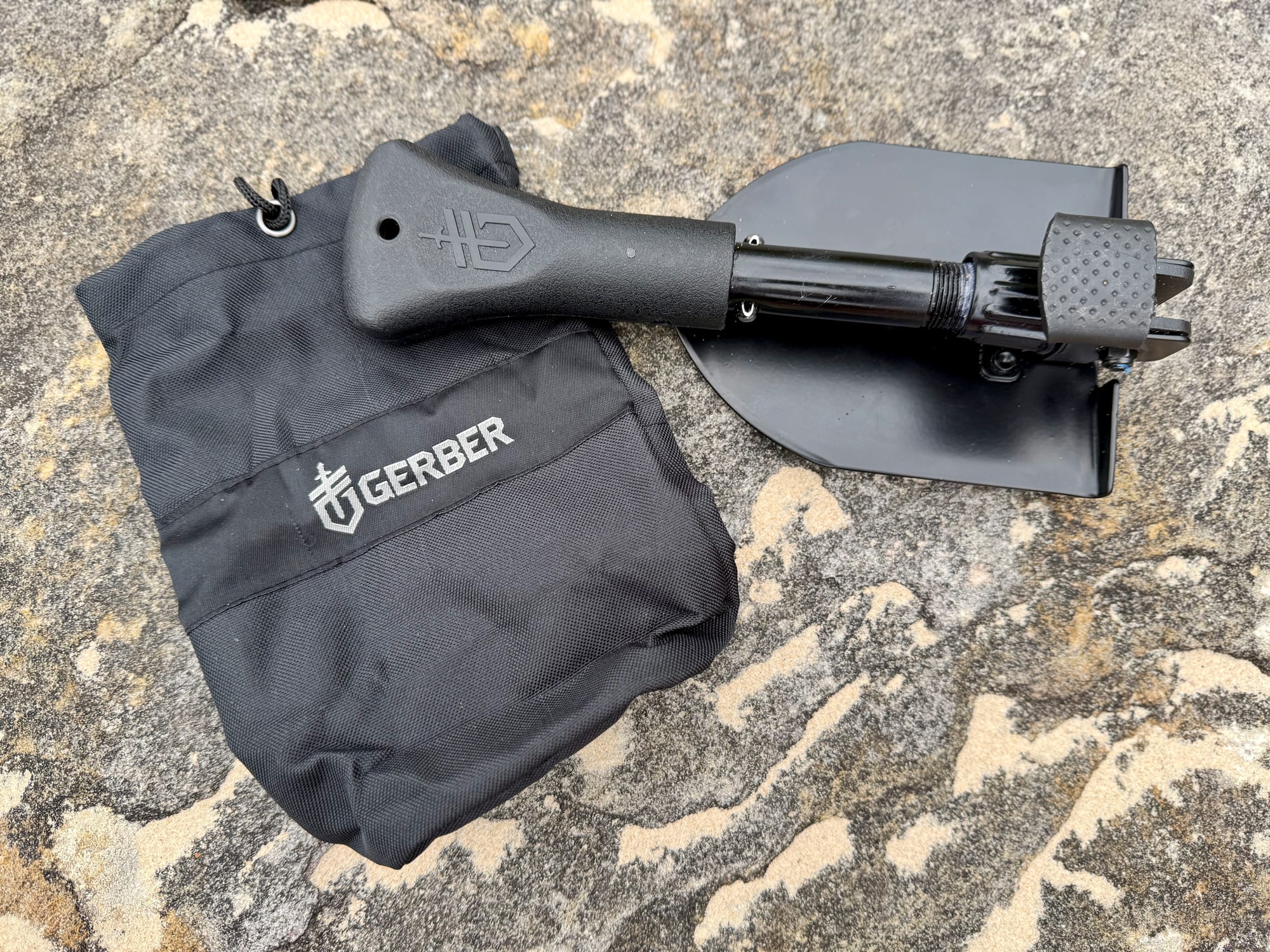 The Gerber Gorge folding shovel folded up, lying on its black drawstring bag