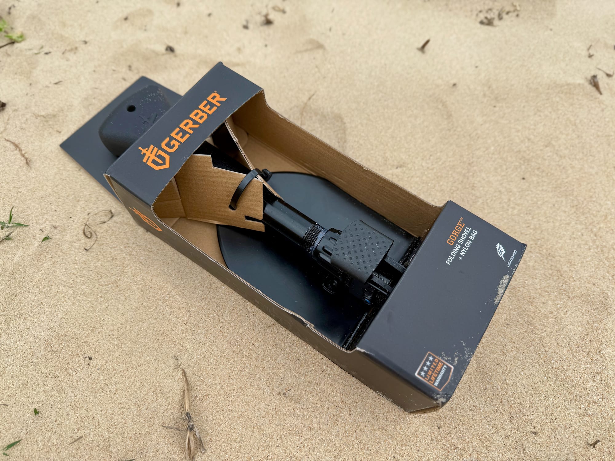 The Gerber Gorge folding shovel in its open box, lying on beach sand