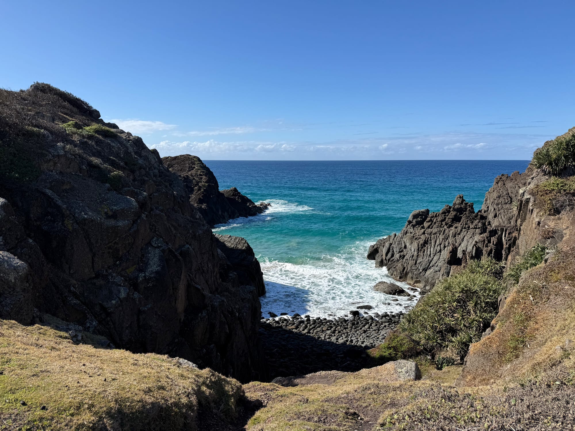 A rocky gully on the headland at Hat Head, with waves breaking onto a pebble beach