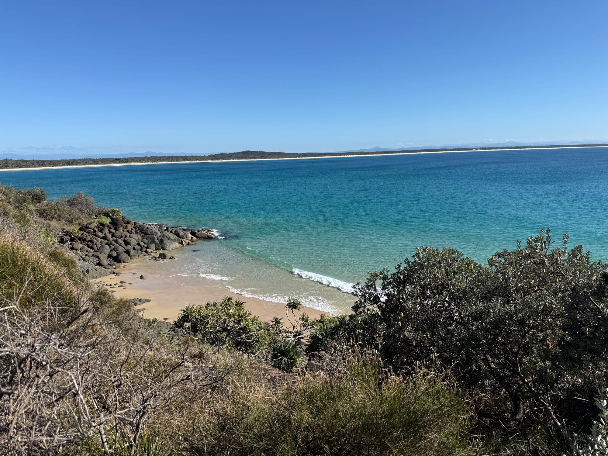 A small sandy beach and rocks below the Korogoro walking track, with turquoise water and the long beach behind