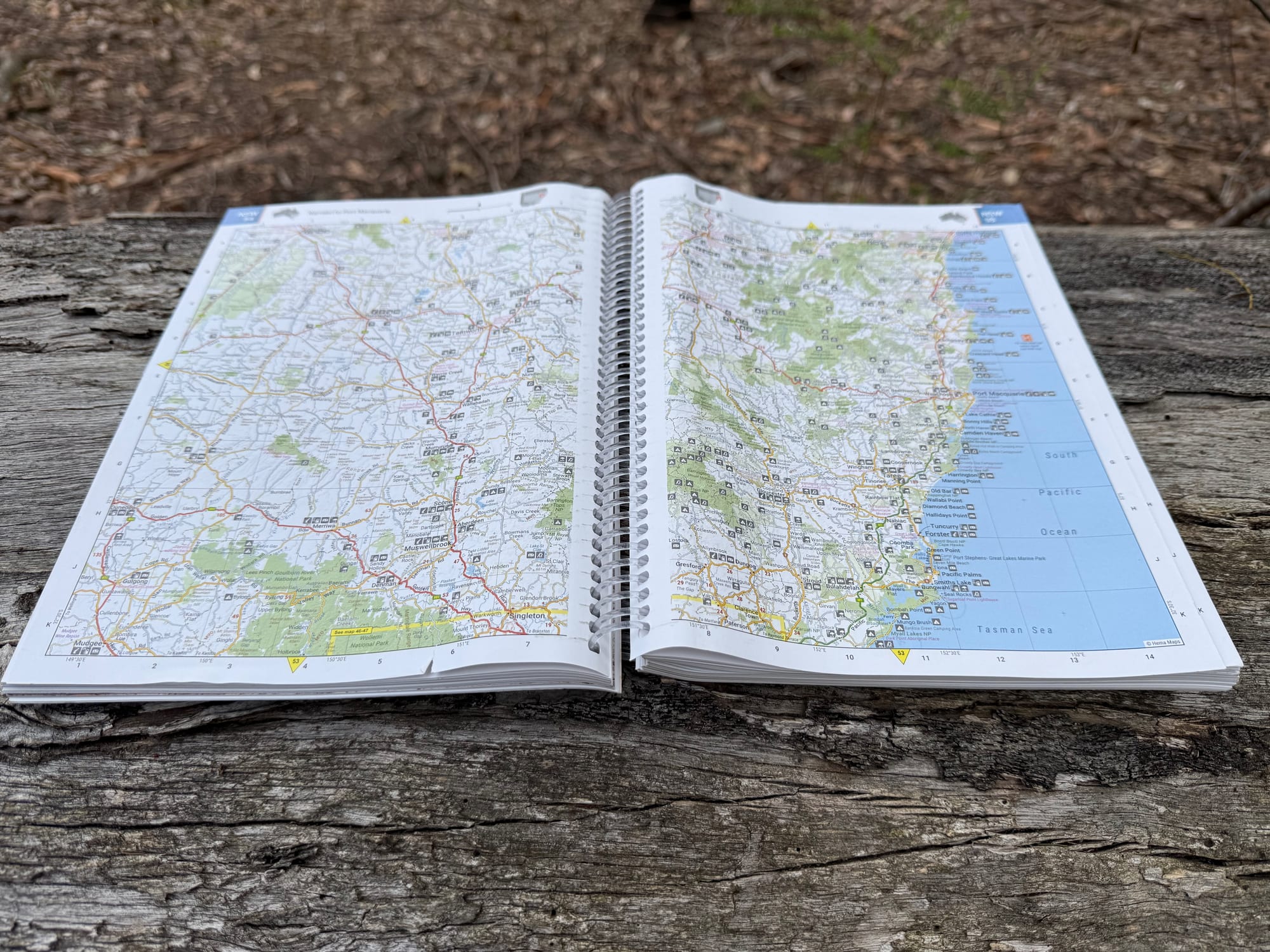 A double page of the Hema Handy Atlas open on a log, showing the NSW coast