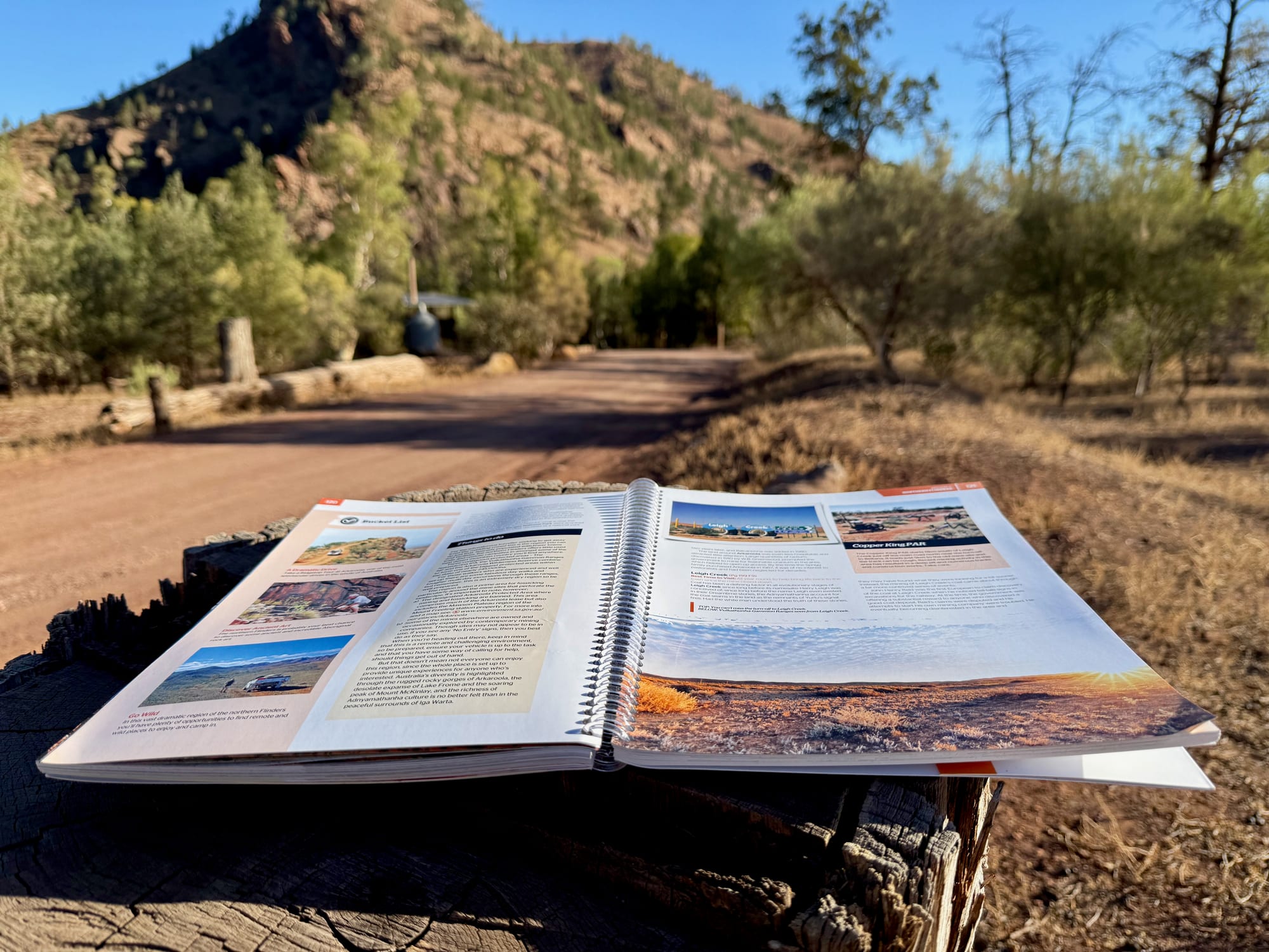 The Hema Flinders Ranges Atlas & Guide lying open on a tree stump at camp