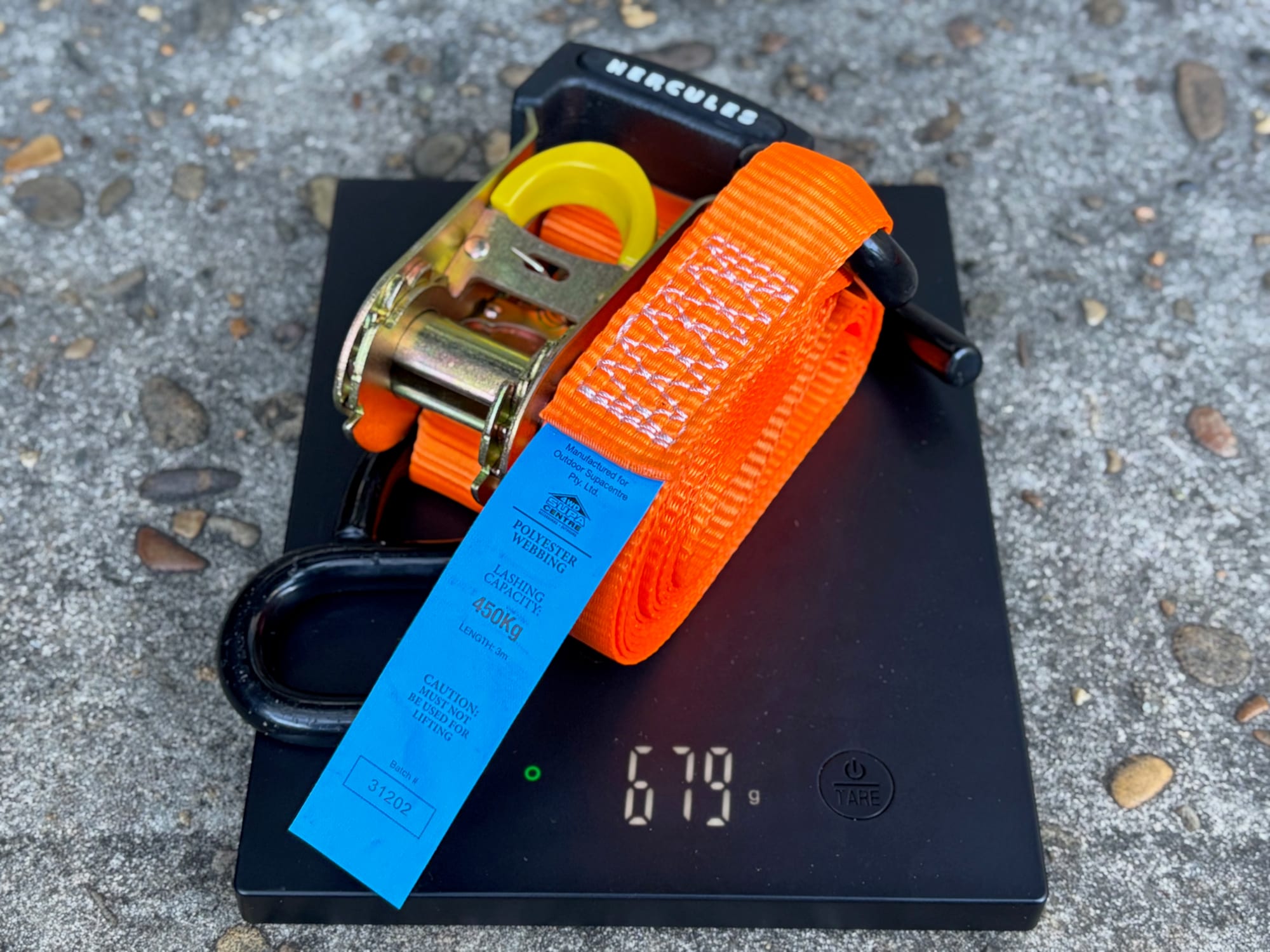 One Hercules ratchet strap rolled up on a scale showing 679 g
