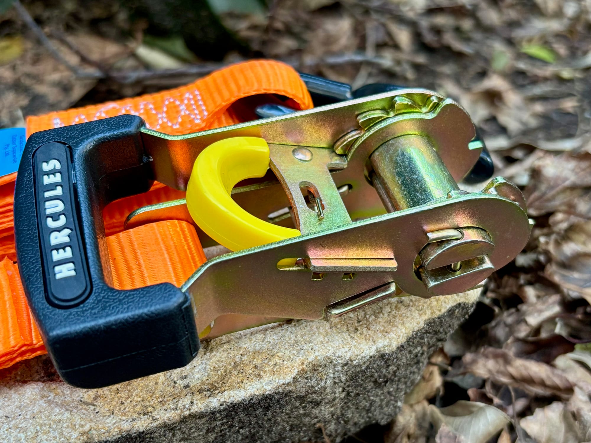 The gold-coloured ratchet of a Hercules strap with its black rubber grip and yellow release lever