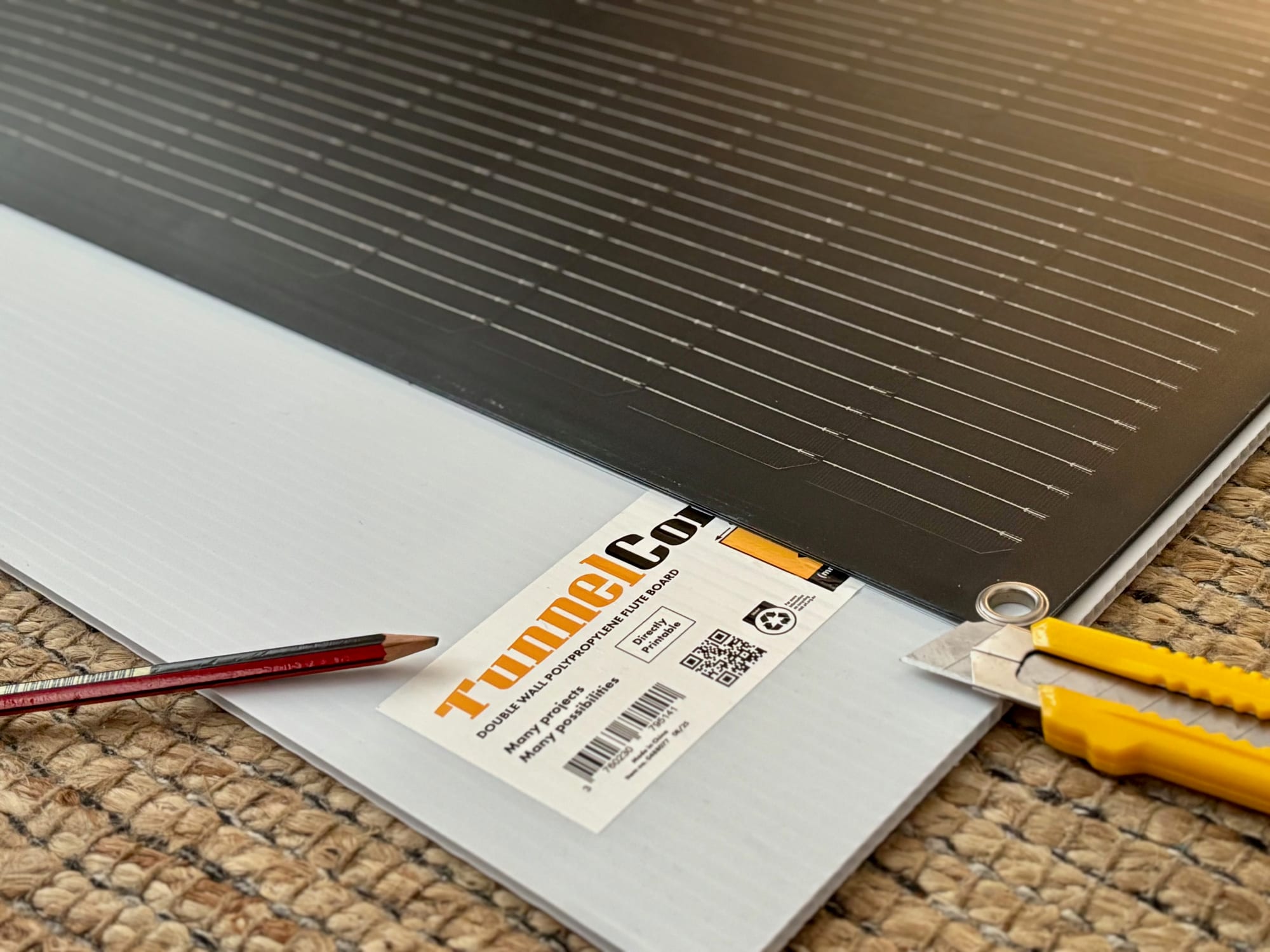 A flexible solar panel on a sheet of corflute, with a pencil and utility knife