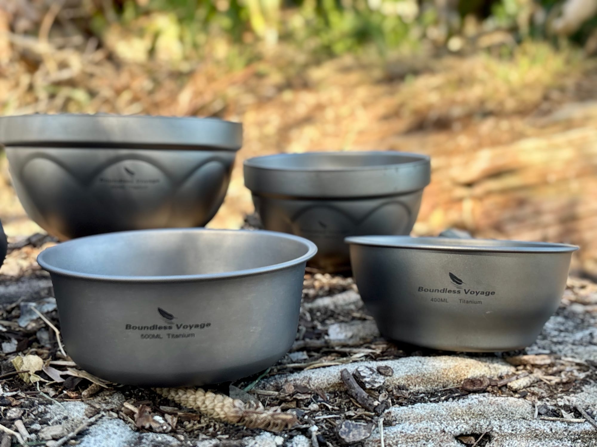Two double-walled titanium bowls with a pressed pattern at the back and two plain single-walled bowls in front, on a rock