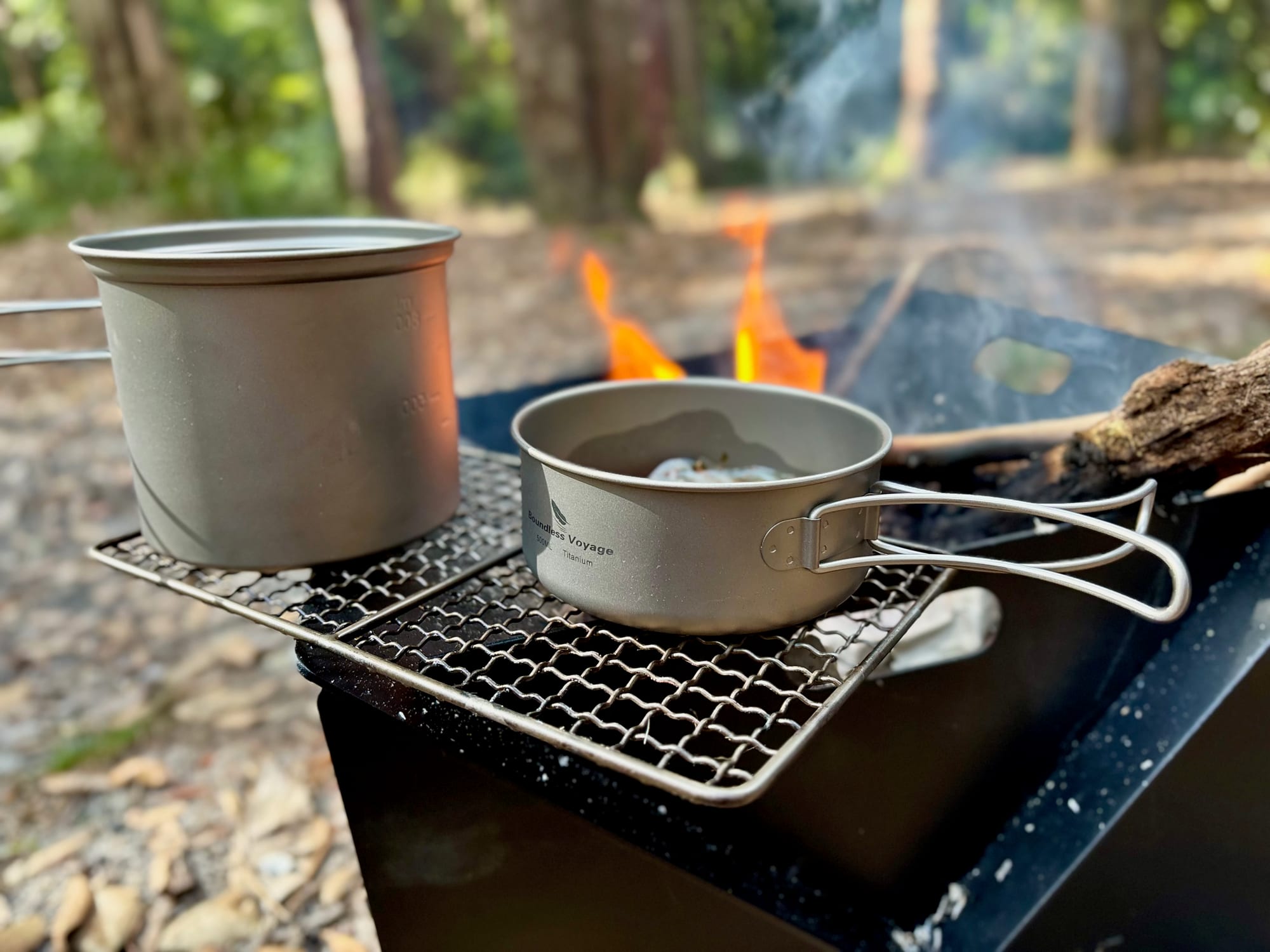 A titanium pot and pan on a grill over a fire, with their folding handles out
