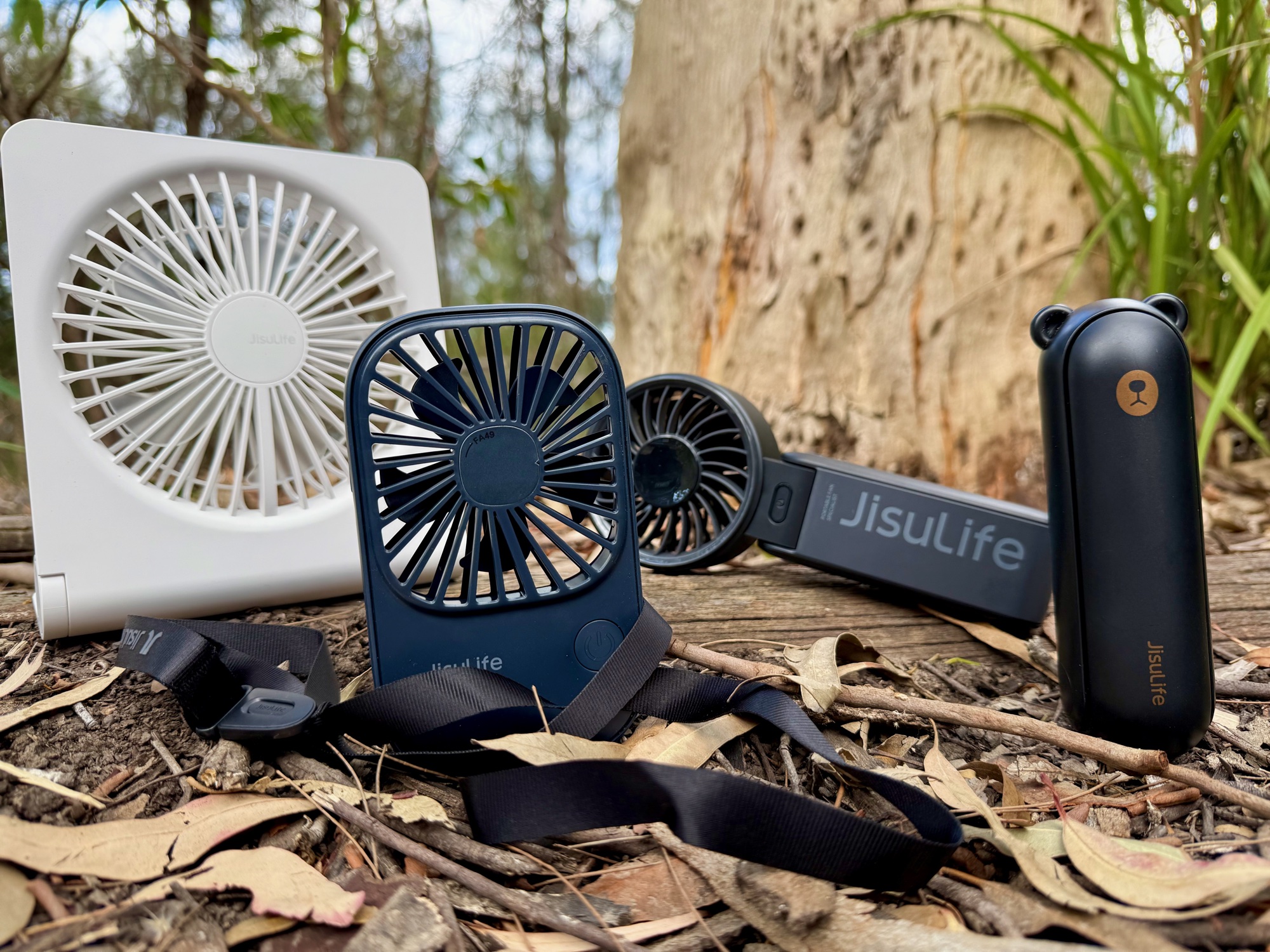 The four JisuLife fans side by side on a log in the bush