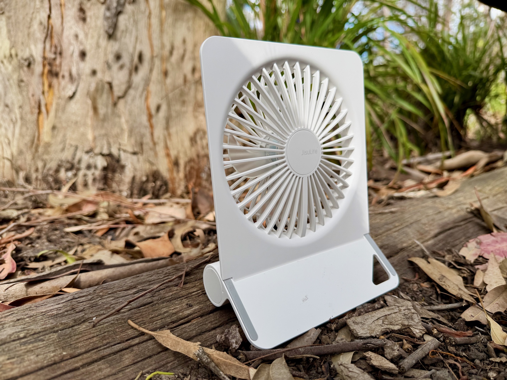 The white JisuLife Table Fan Life3 standing on a log in the bush