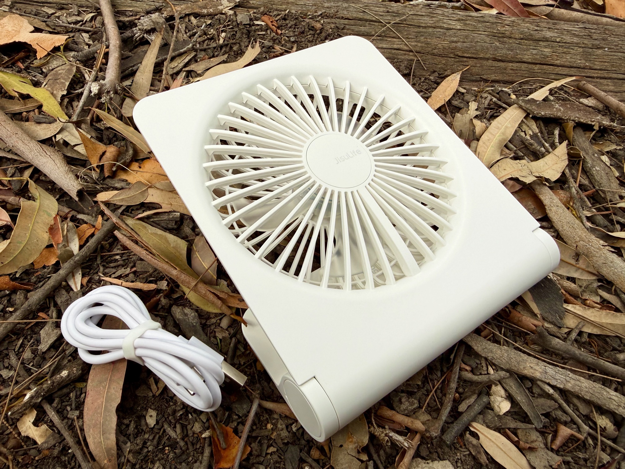 The white JisuLife Table Fan Life3 with its USB-C cable on leaf litter