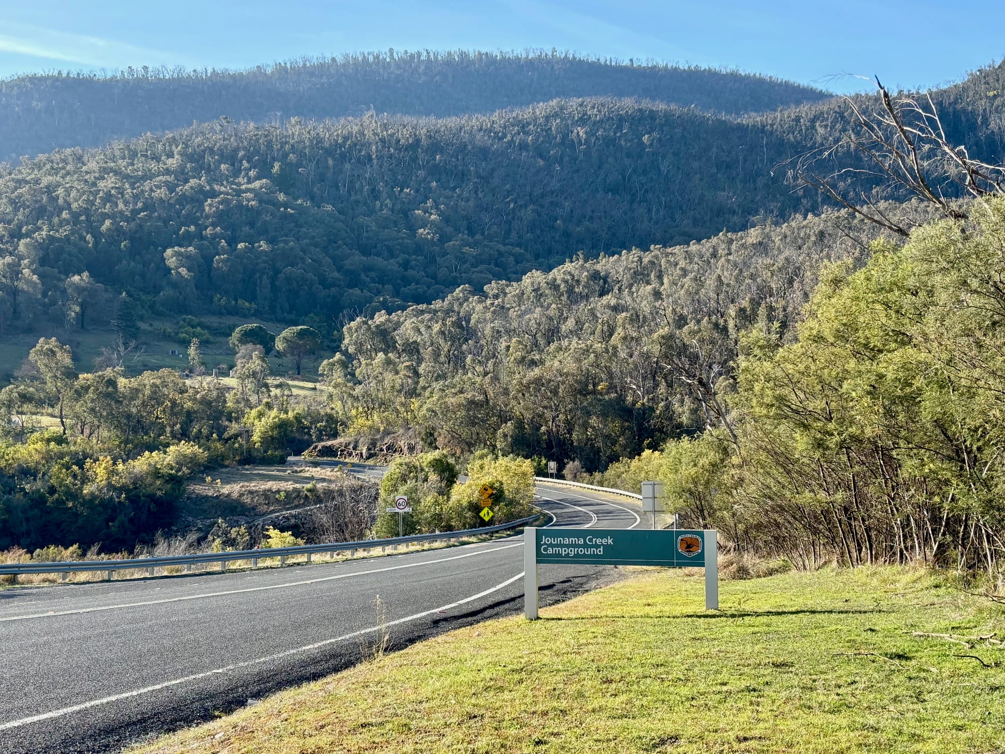 The Jounama Creek Campground sign beside the Snowy Mountains Highway, with forested hills behind