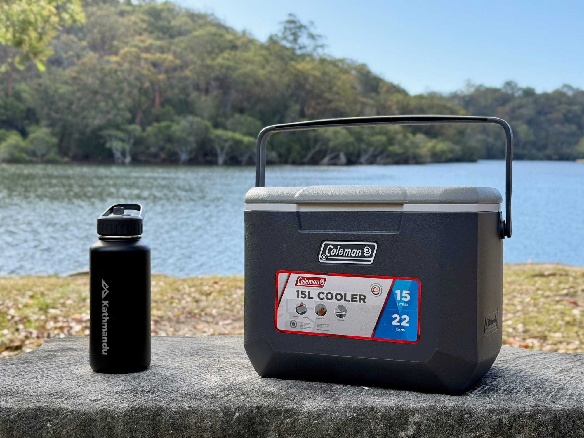 The Kathmandu bottle next to a Coleman 15L hard cooler by the lake