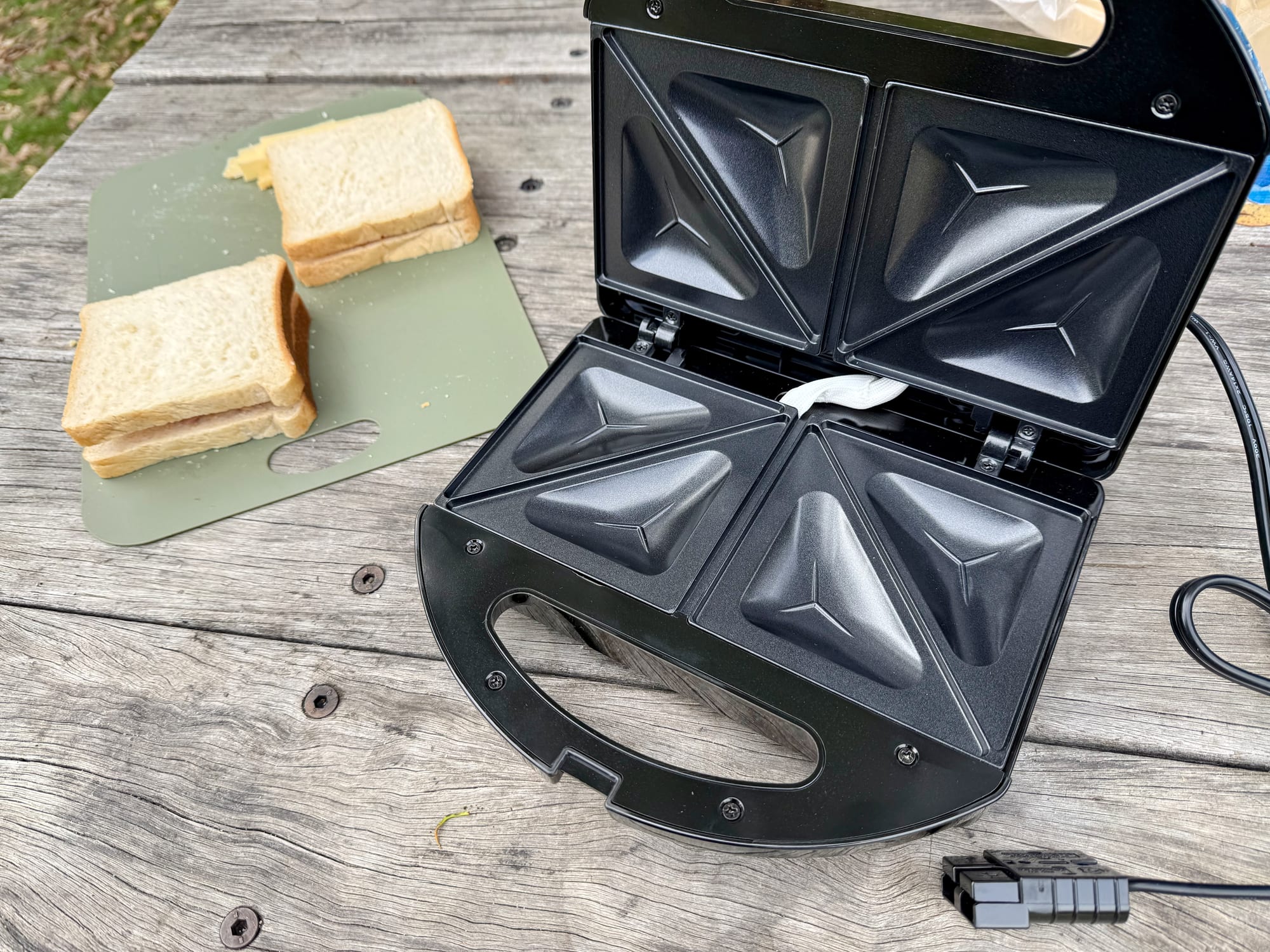 The KickAss jaffle maker open, showing its two non-stick triangle plates, next to two sandwiches