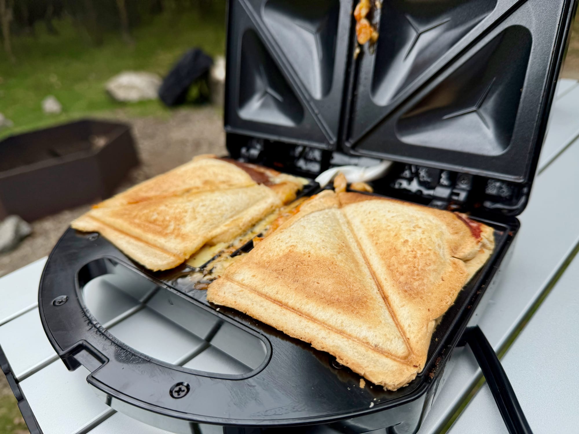 Two golden jaffles in the open KickAss jaffle maker on the camp table