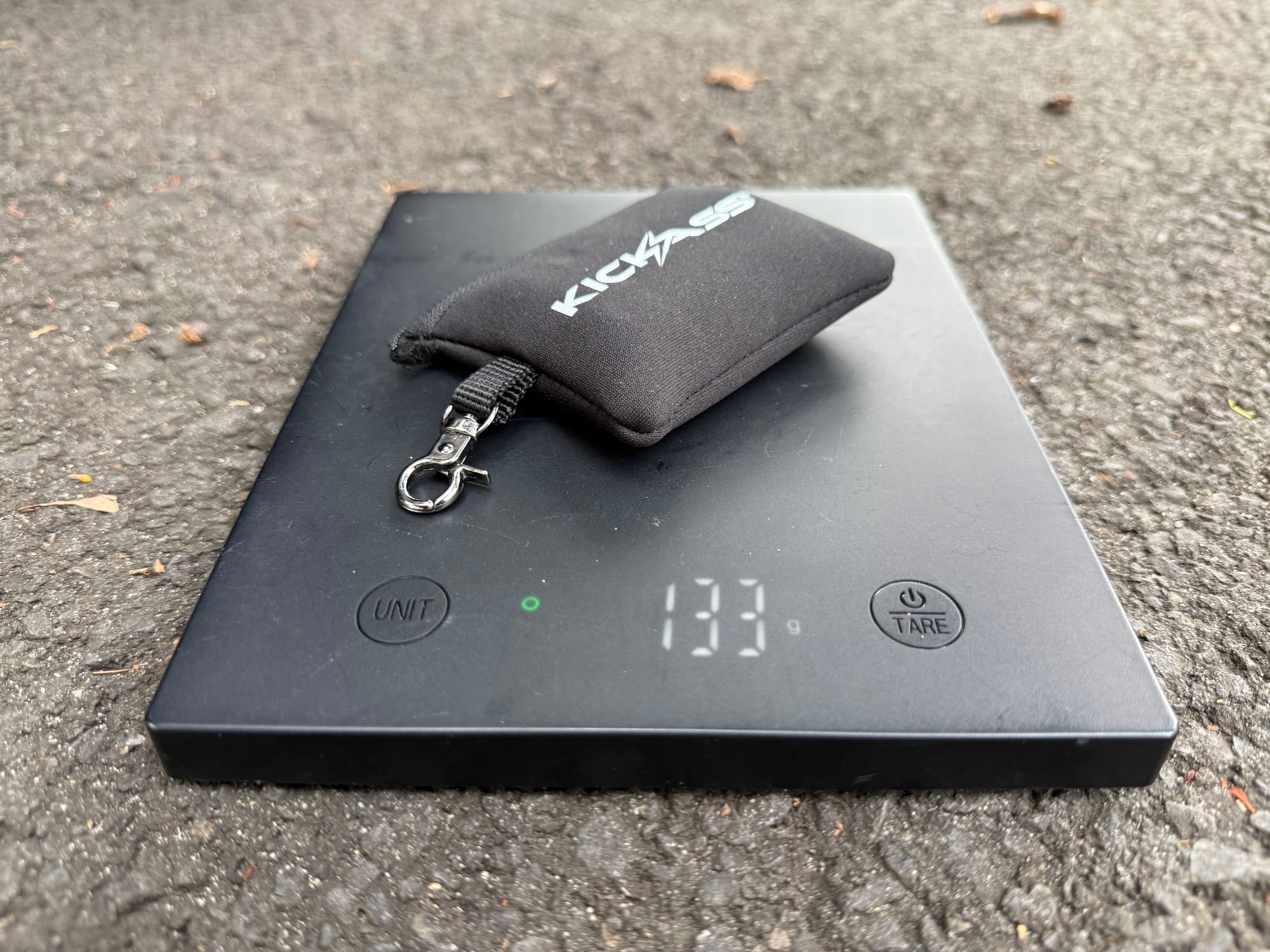 The KickAss deflator set in its pouch on a digital scale showing 133 grams