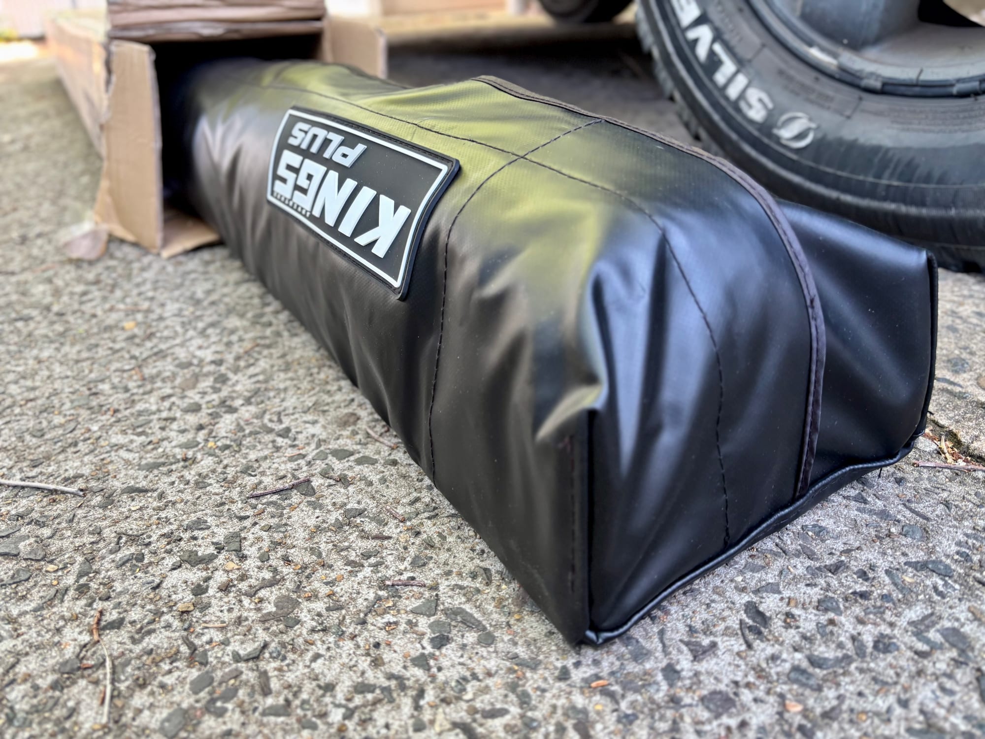 The black Kings Plus awning bag on the ground next to a 4WD wheel
