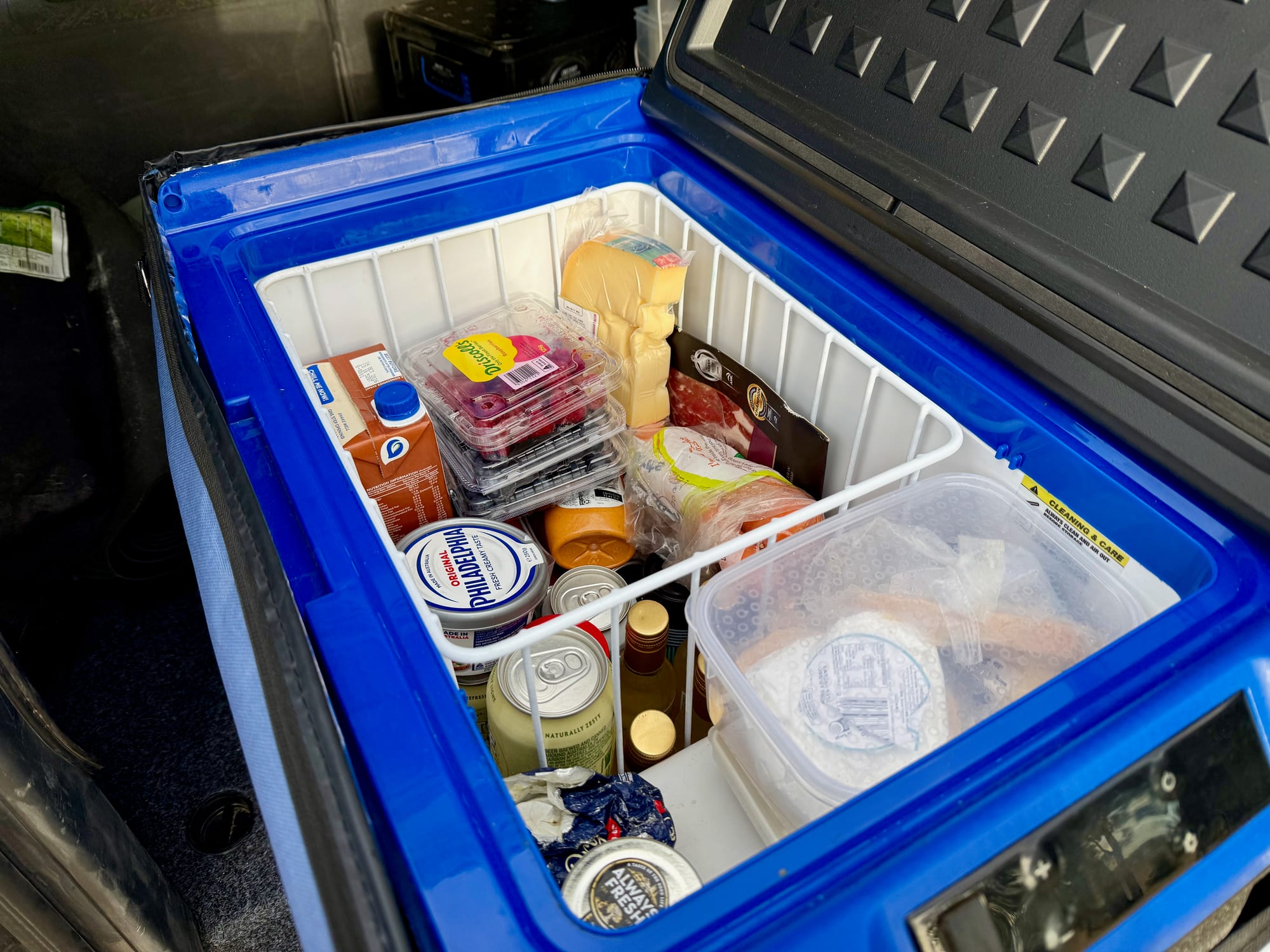 The packed Kings 40L fridge: berries, cheese, milk and cans in the wire basket, a container on the little shelf at the front