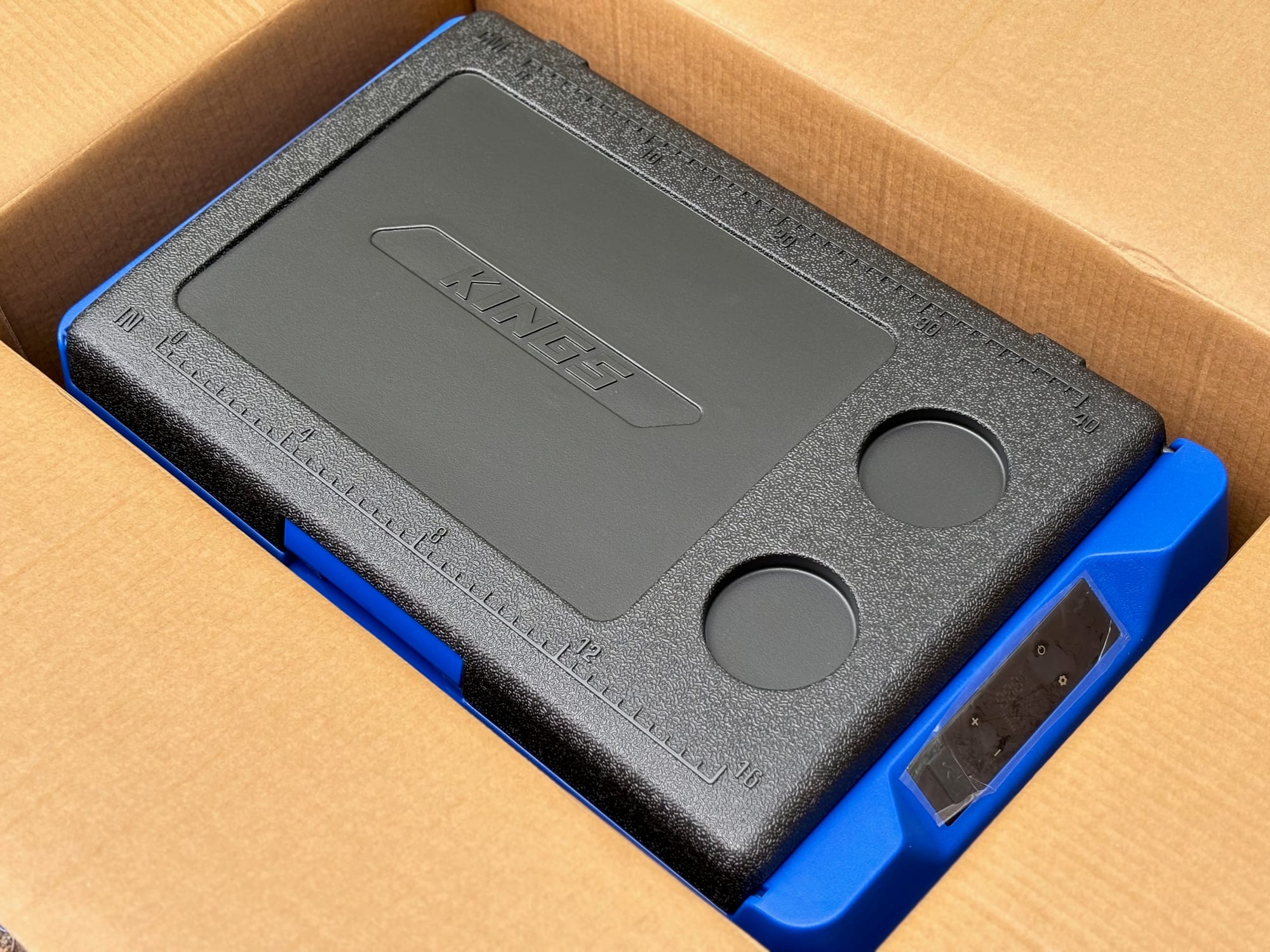 The lid of the new Kings Escape 40 fridge in its box, with two cup holders and a ruler in cm and inches