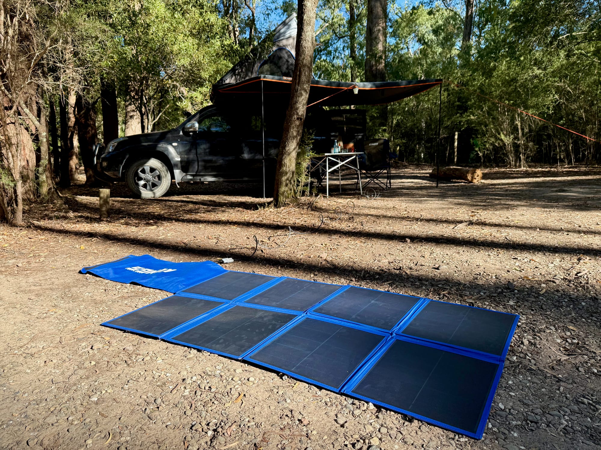 The Kings 240W solar blanket lying in the sun on the ground, with the extension lead running to a 4WD parked in the shade under the trees