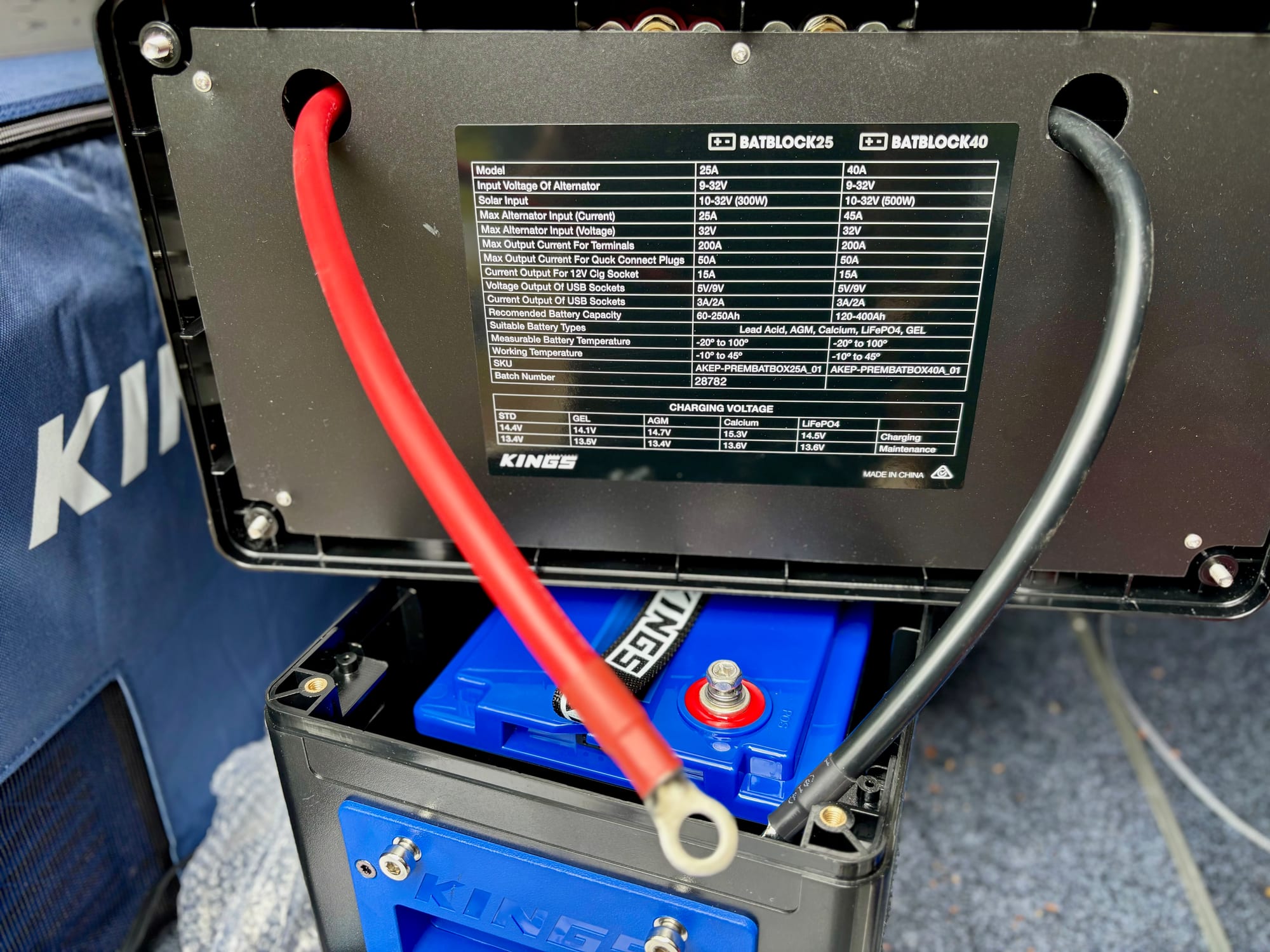 The lid of the BatBlock lifted, with the red and black cables bolted to the battery terminals and the spec label underneath