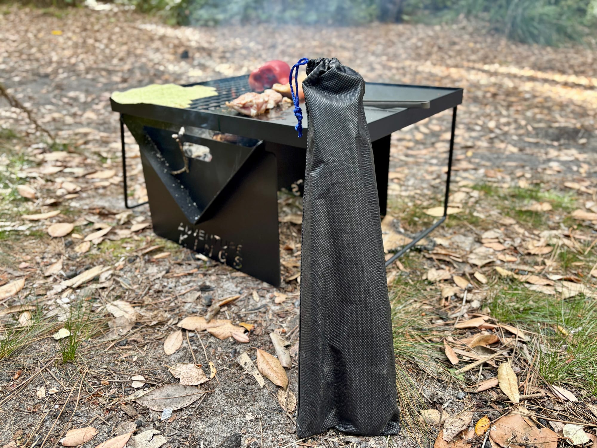 The Kings BBQ Tool Set in its drawstring pouch, leaning against the fire pit