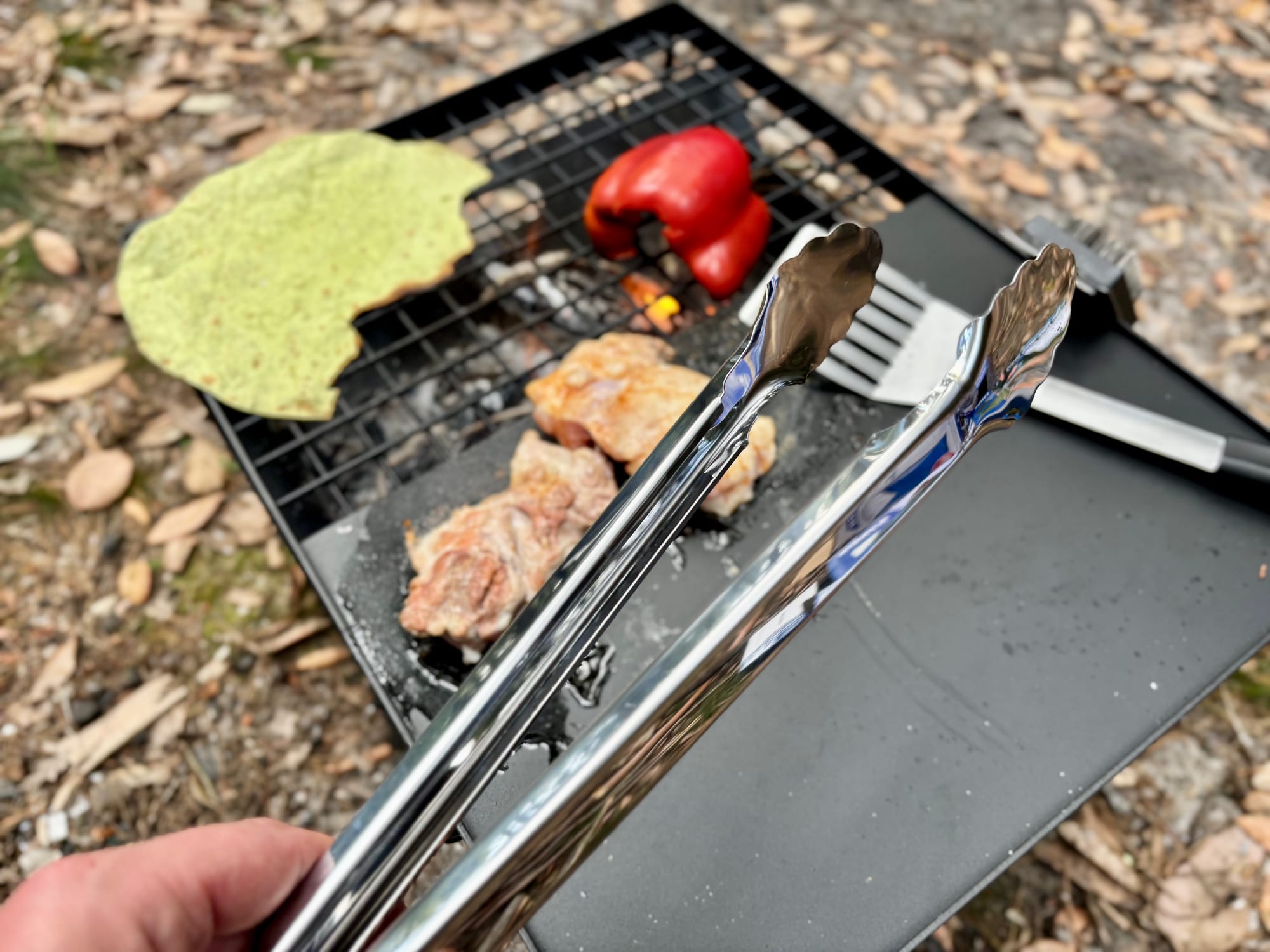 The Kings tongs held over the hotplate, next to chicken on the grill