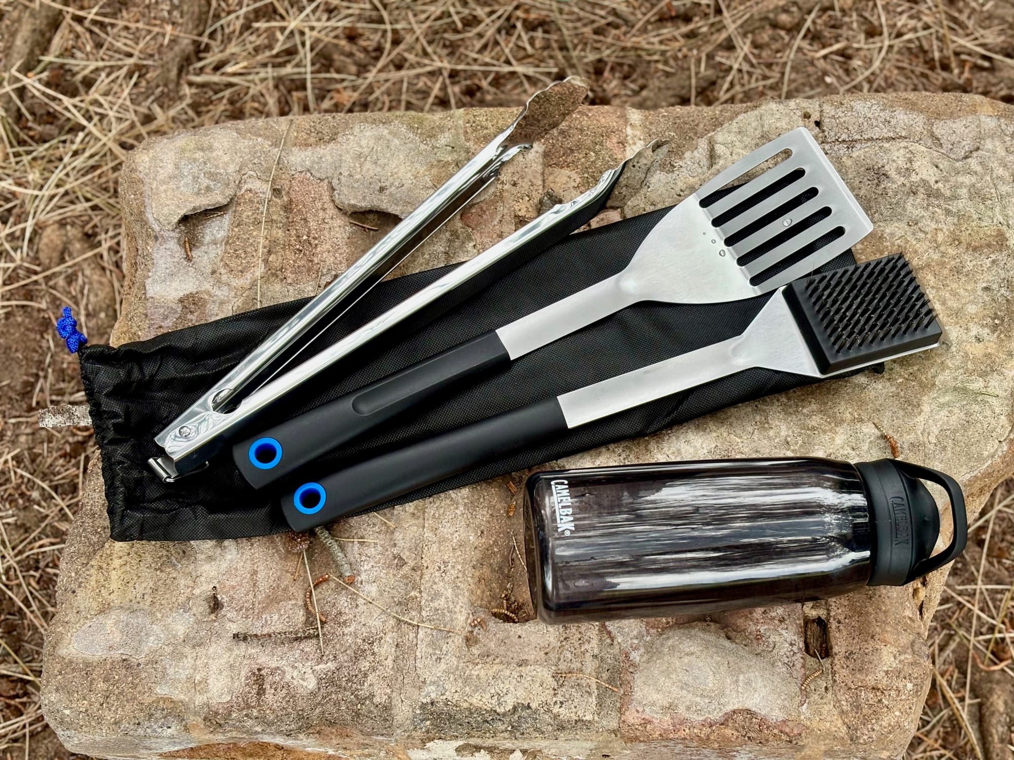 The tongs, spatula and brush of the Kings BBQ Tool Set laid out on their pouch, next to a water bottle for size
