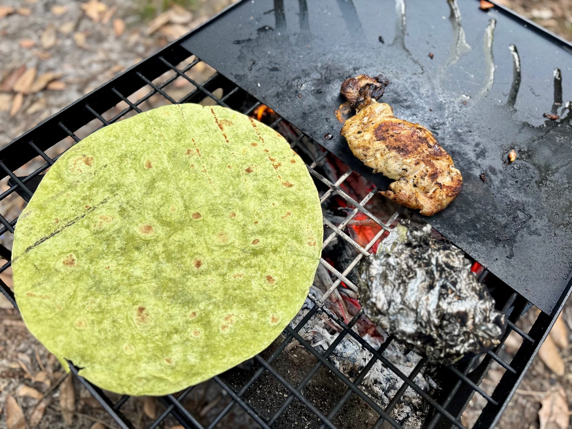 A wrap warming on the grill next to cooked chicken on the hotplate
