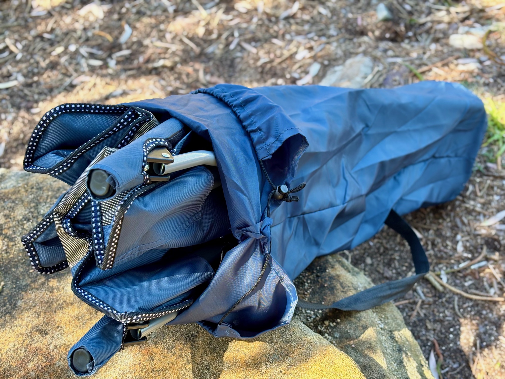 The folded Kings Deluxe Armchair going into its drawstring bag on a rock