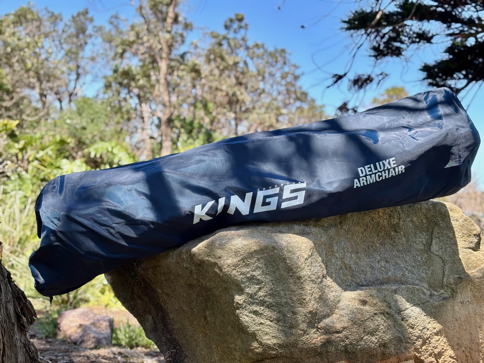 The Kings Deluxe Armchair packed in its long blue carry bag on a rock