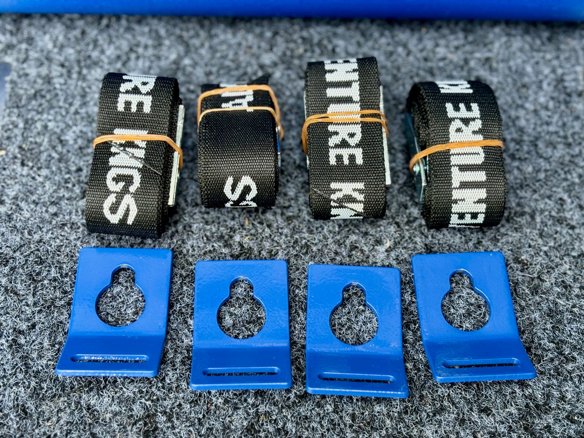 The four Kings tie-down straps rolled up above the four blue steel brackets with keyhole slots