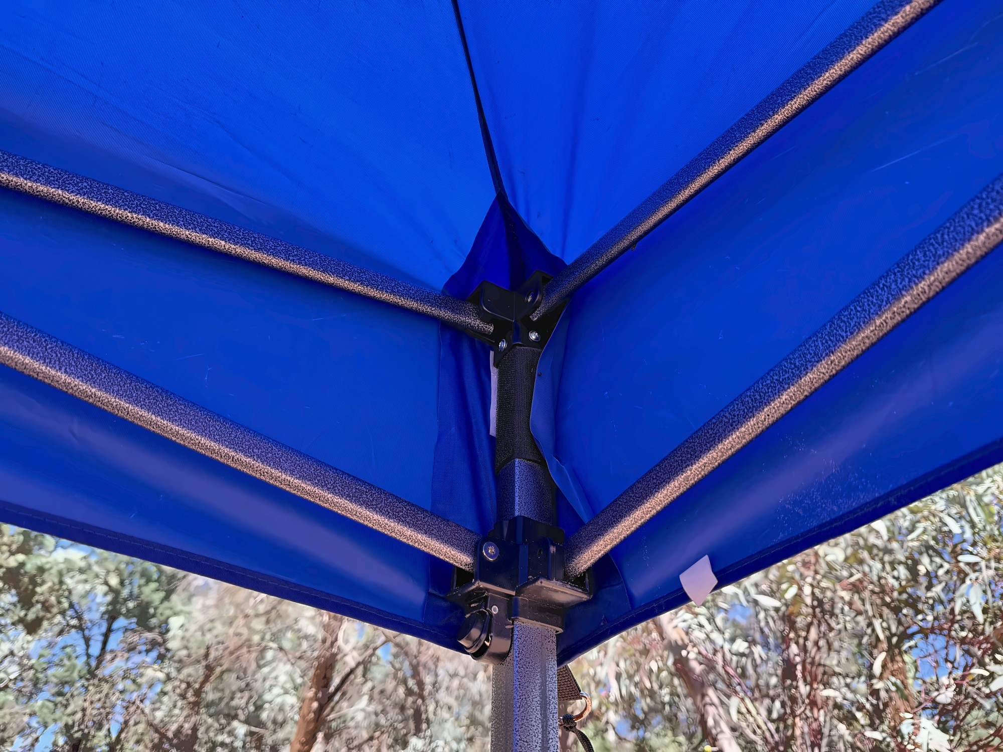 A corner joint of the Kings gazebo seen from below, with the hammertone steel frame under the blue canopy
