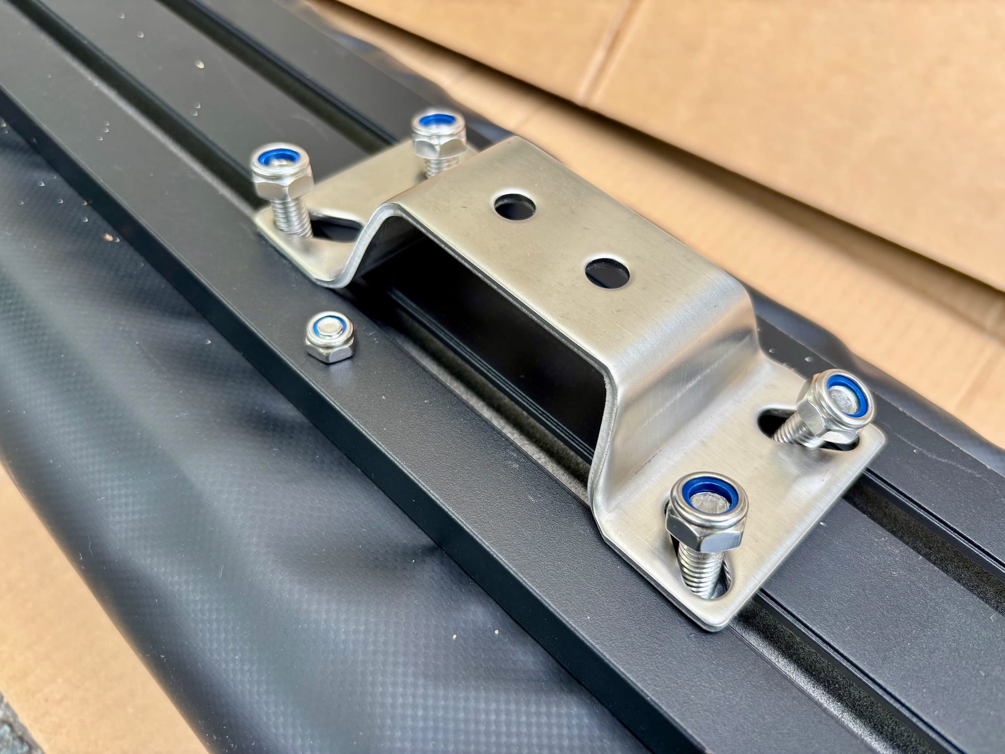 A stainless awning bracket bolted onto the track of a rolled-up awning with blue nyloc nuts