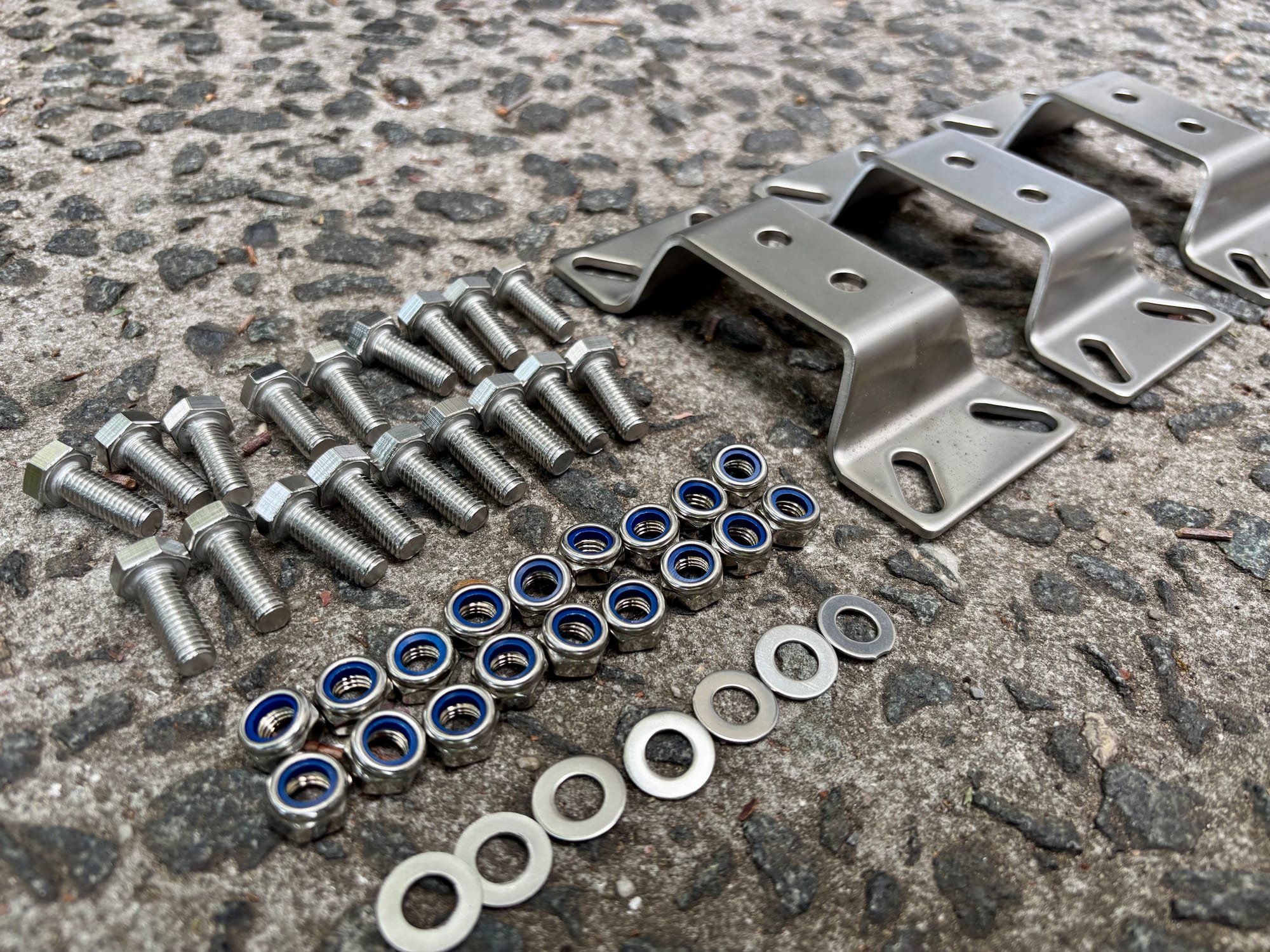 Stainless bolts, blue nyloc nuts and washers laid out in rows in front of the three stainless awning brackets