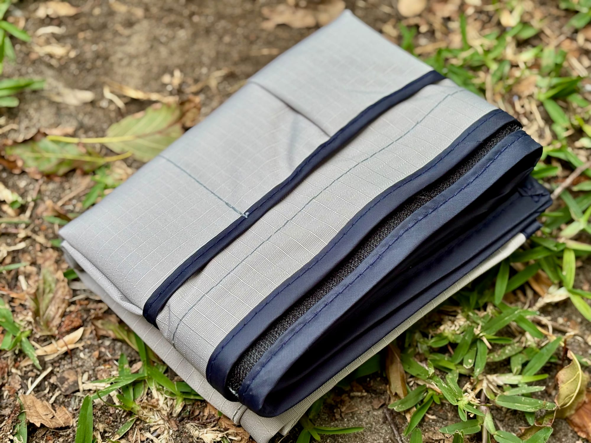 The storage pocket folded on the grass, with the navy binding and the Velcro edge on top