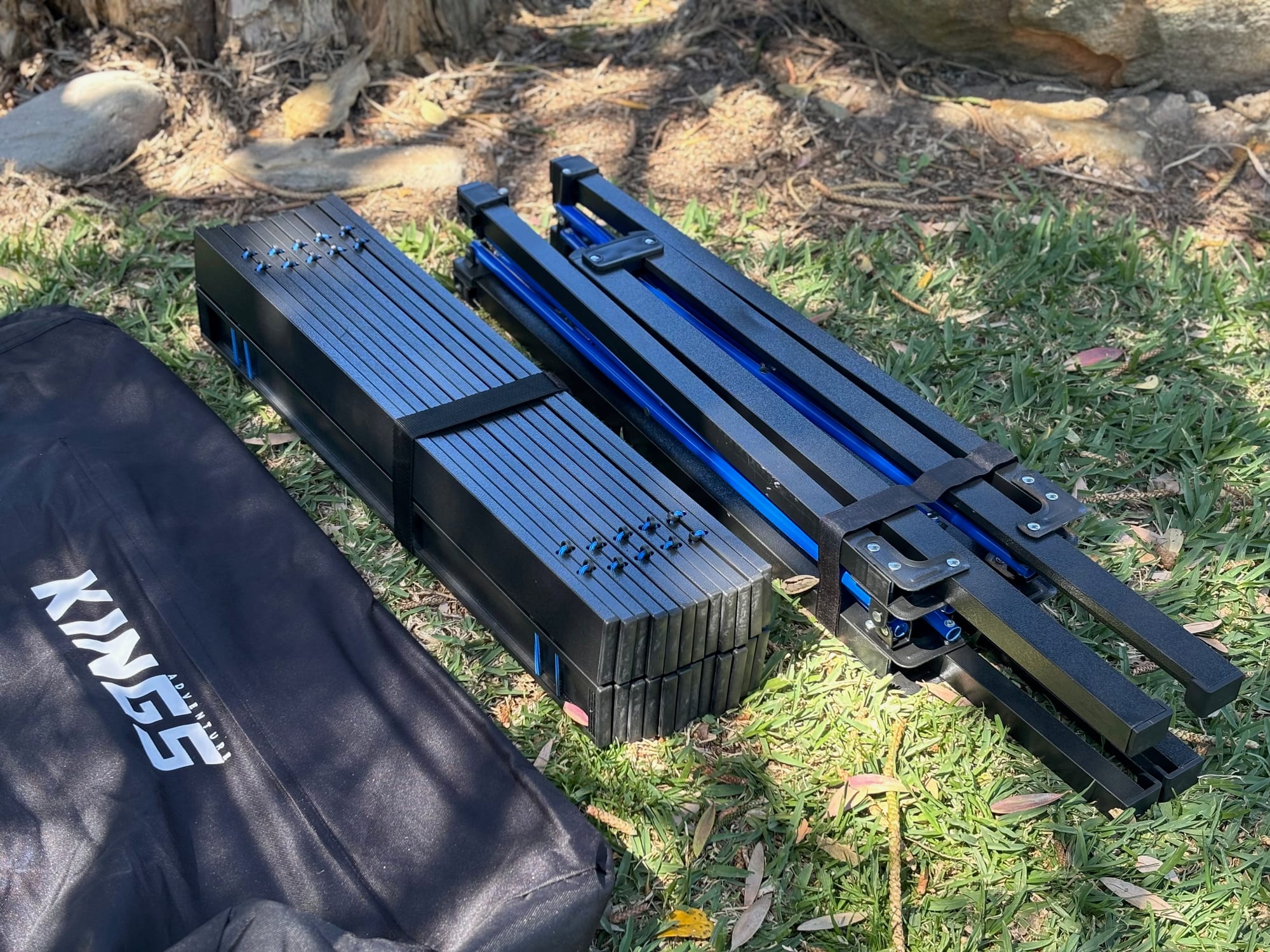 The Kings Large table’s rolled-up slat top and folded steel frame next to its carry bag