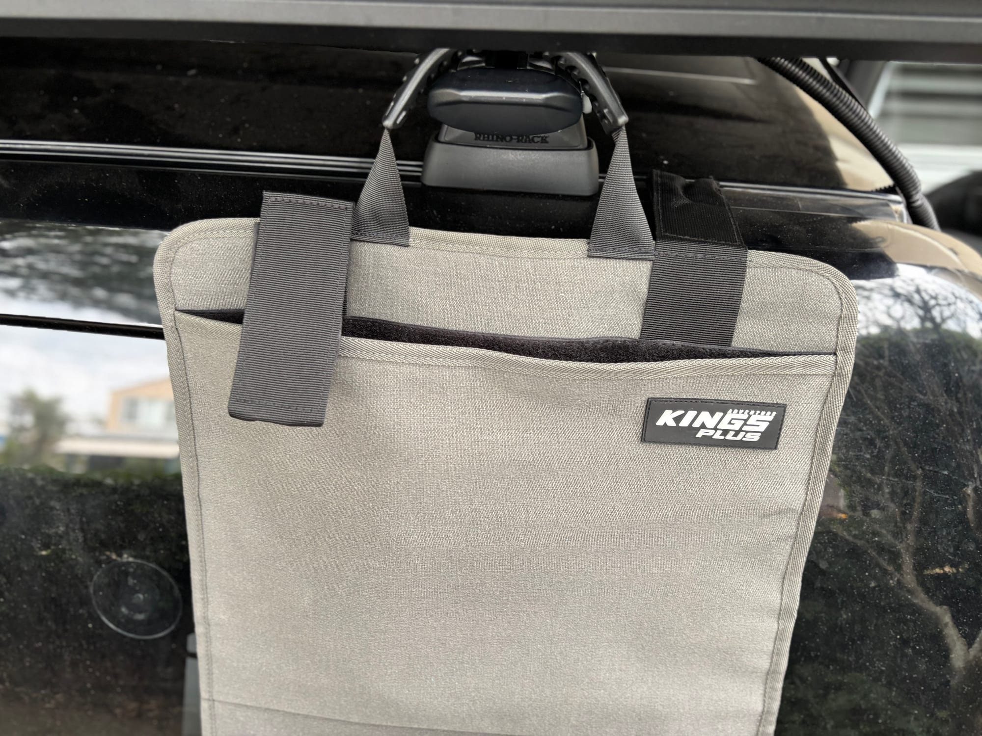 The Kings Plus Hanging Camp Caddy folded up and hanging by its handles, with the Kings Plus patch on the grey canvas