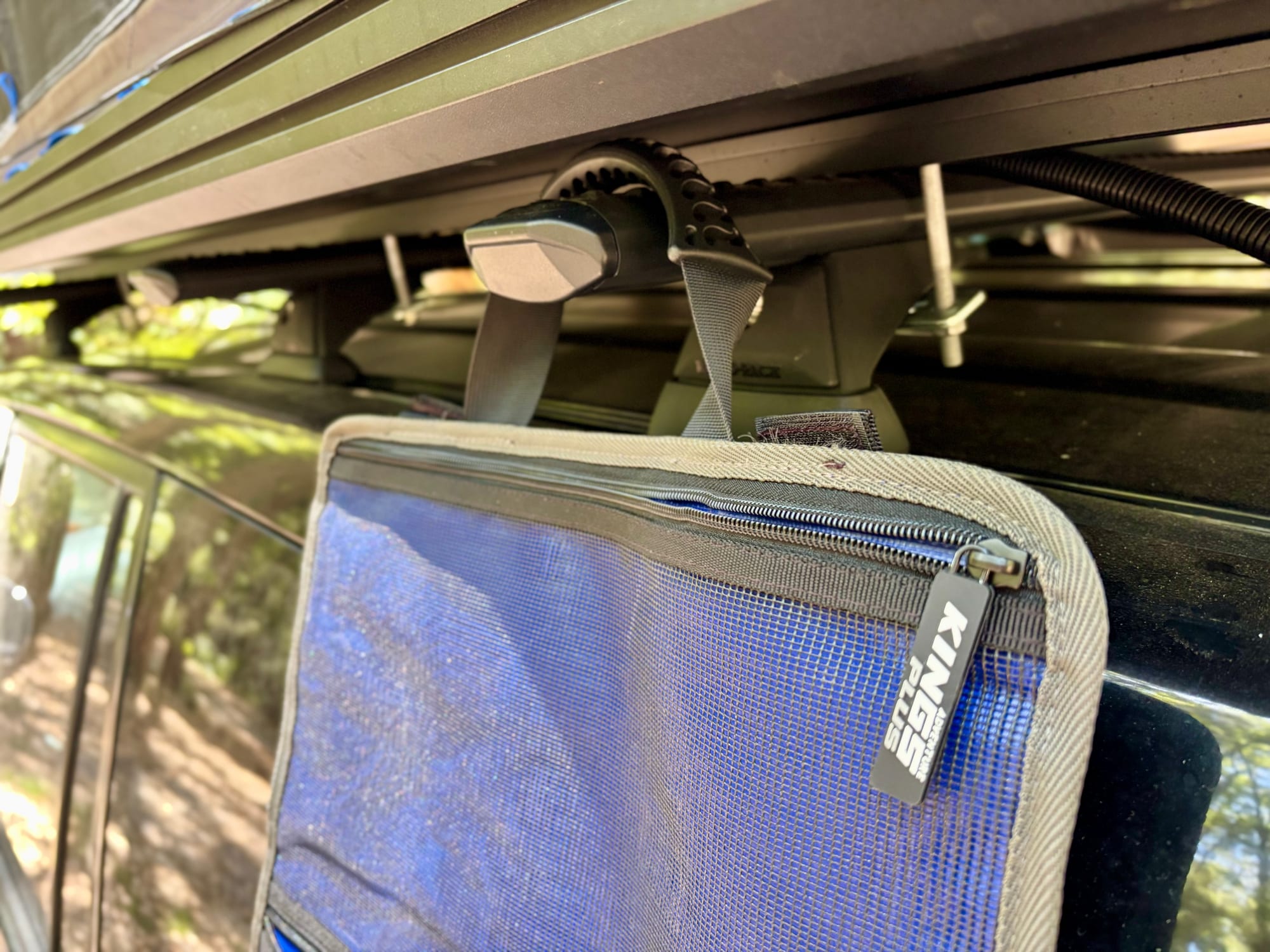 The two handles of the Kings Plus Hanging Camp Caddy hooked over the awning bracket on a roof rack