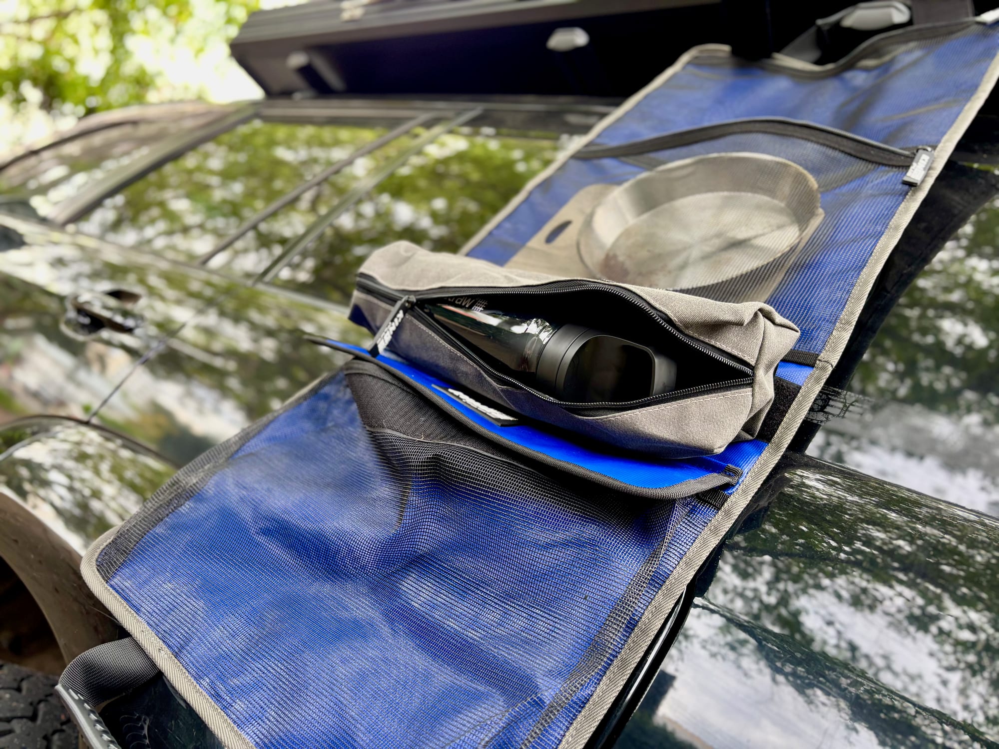 The Kings Plus Hanging Camp Caddy hanging from the side of a 4WD, with plates in the top pocket and the zip bag open