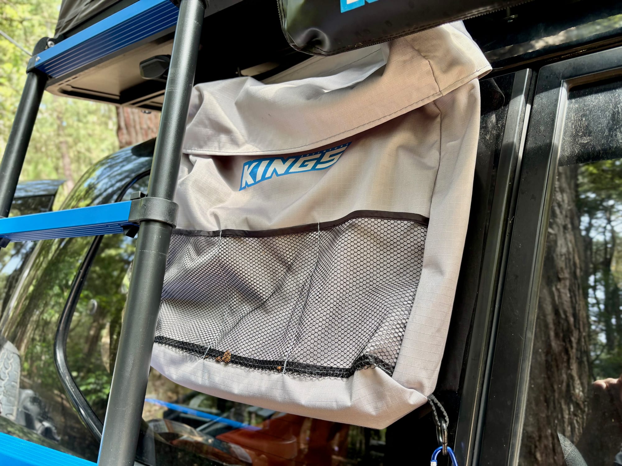 The Kings Universal Storage Bag hanging from the rooftop tent beside the ladder, under the rolled-up awning