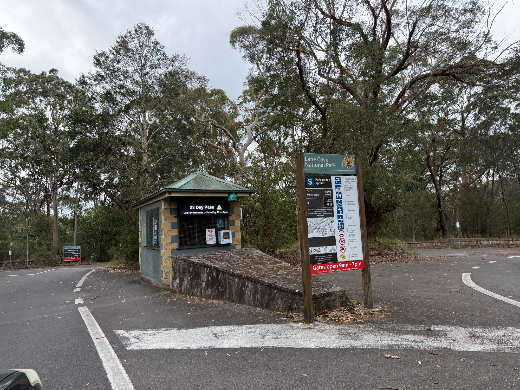 The pay booth and park sign at the entry to Lane Cove National Park, with the road leading into the bush