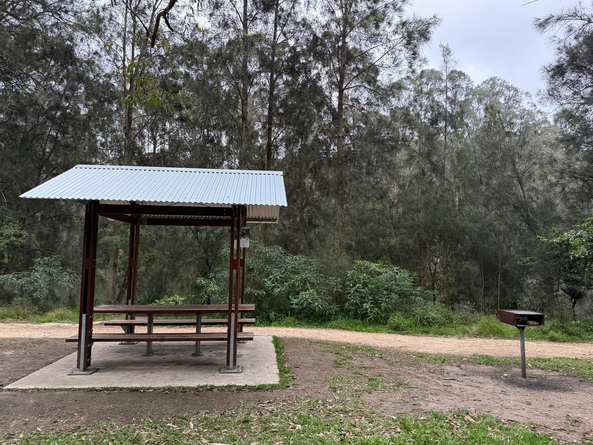 A covered picnic table and a barbecue beside a path at one of the riverside picnic areas